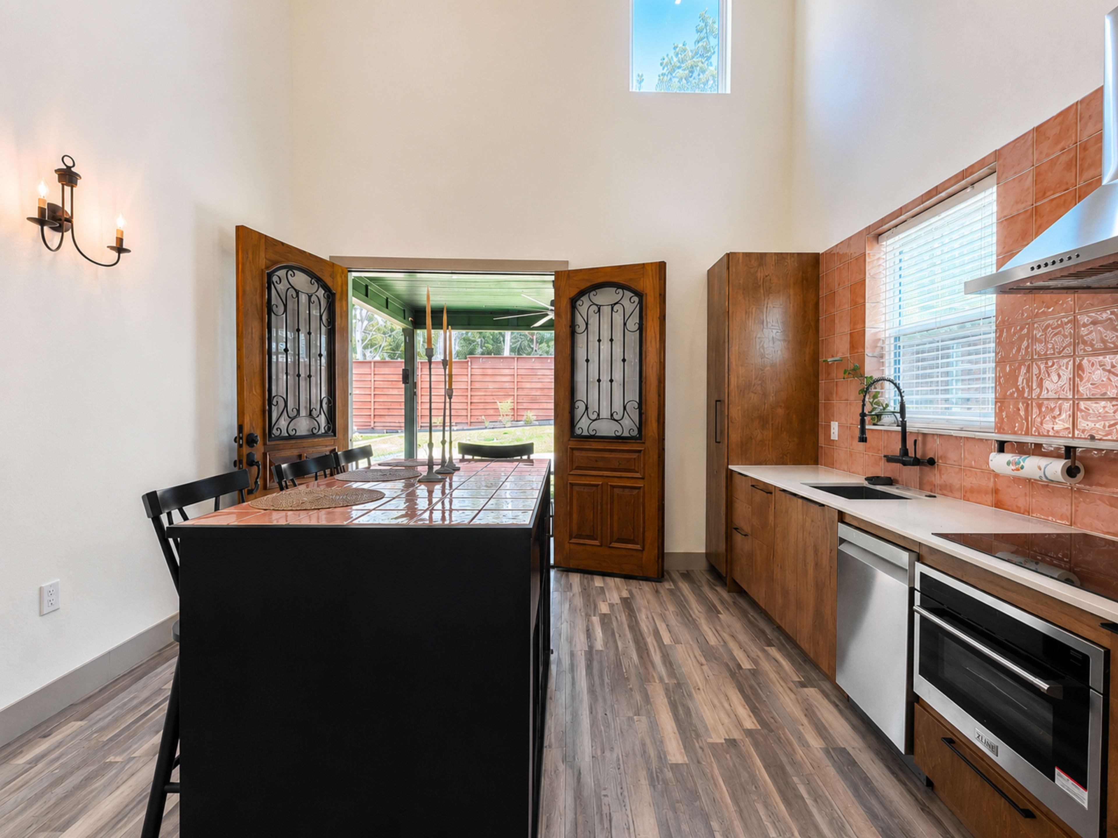 A modern kitchen features a black island, wooden cabinetry, and double doors leading to an outdoor space.