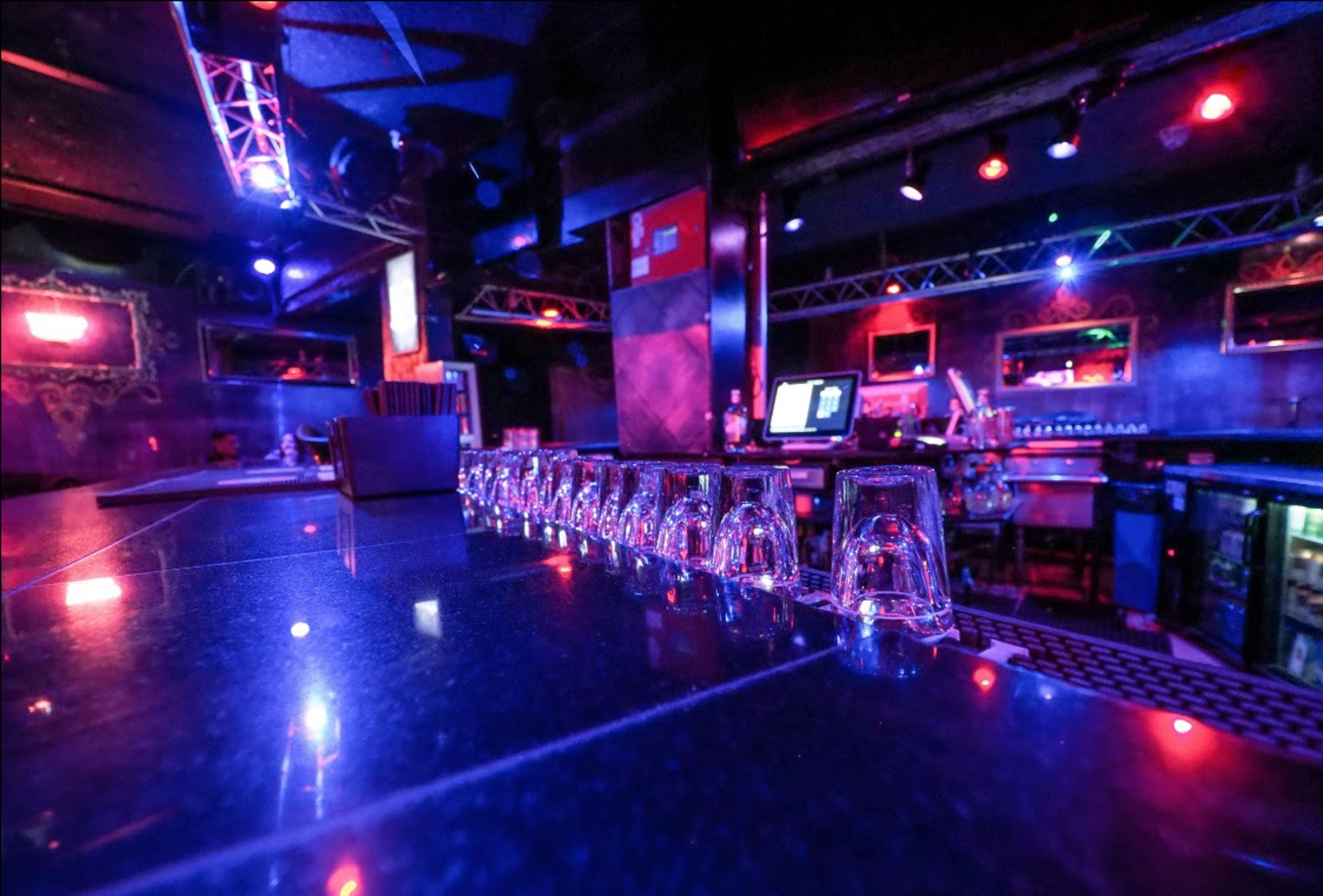 A dimly lit bar with stacked glasses and colorful lighting effects illuminating the space.