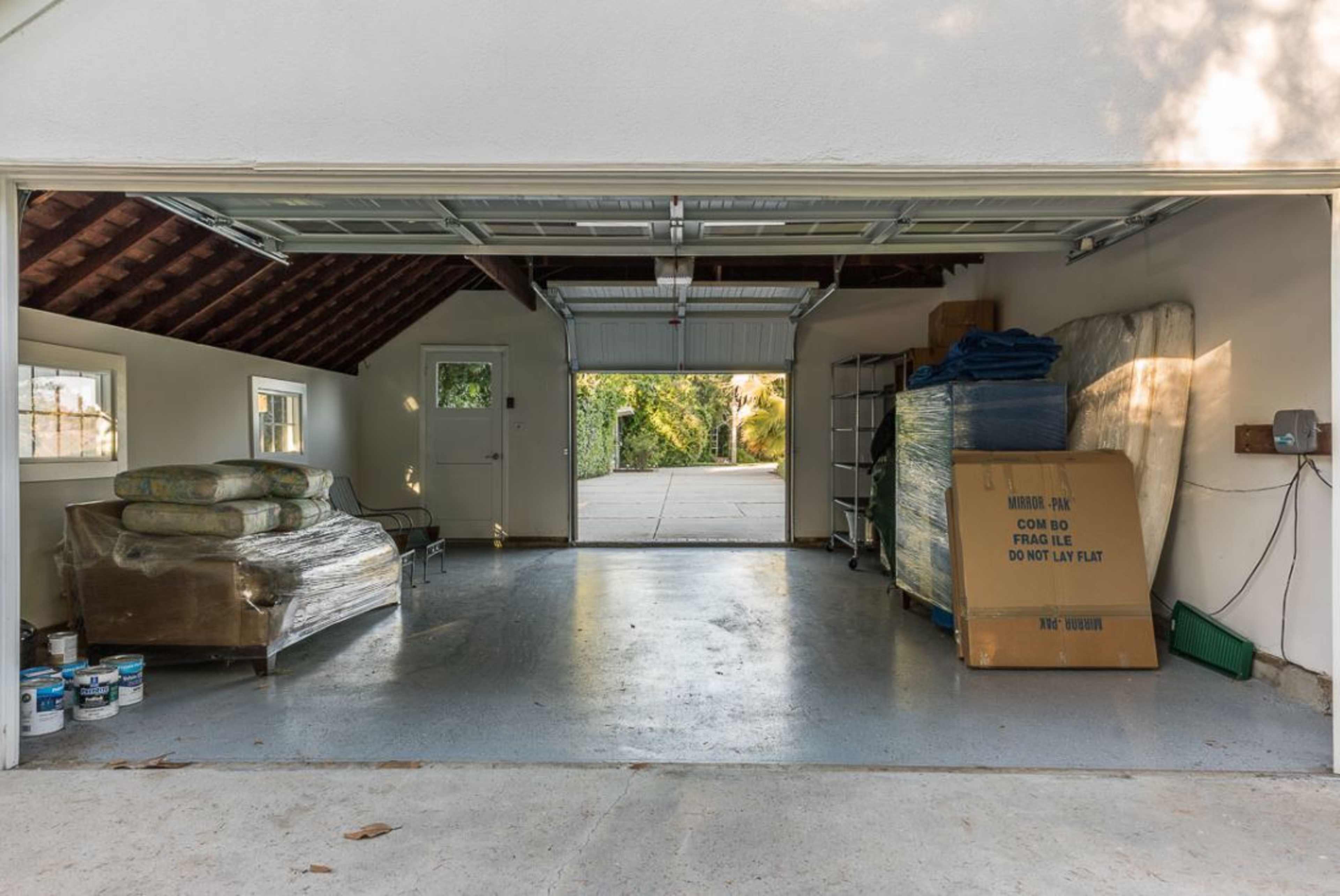 A garage with an open door, revealing stacks of items including mattresses, boxes, and paint cans inside.