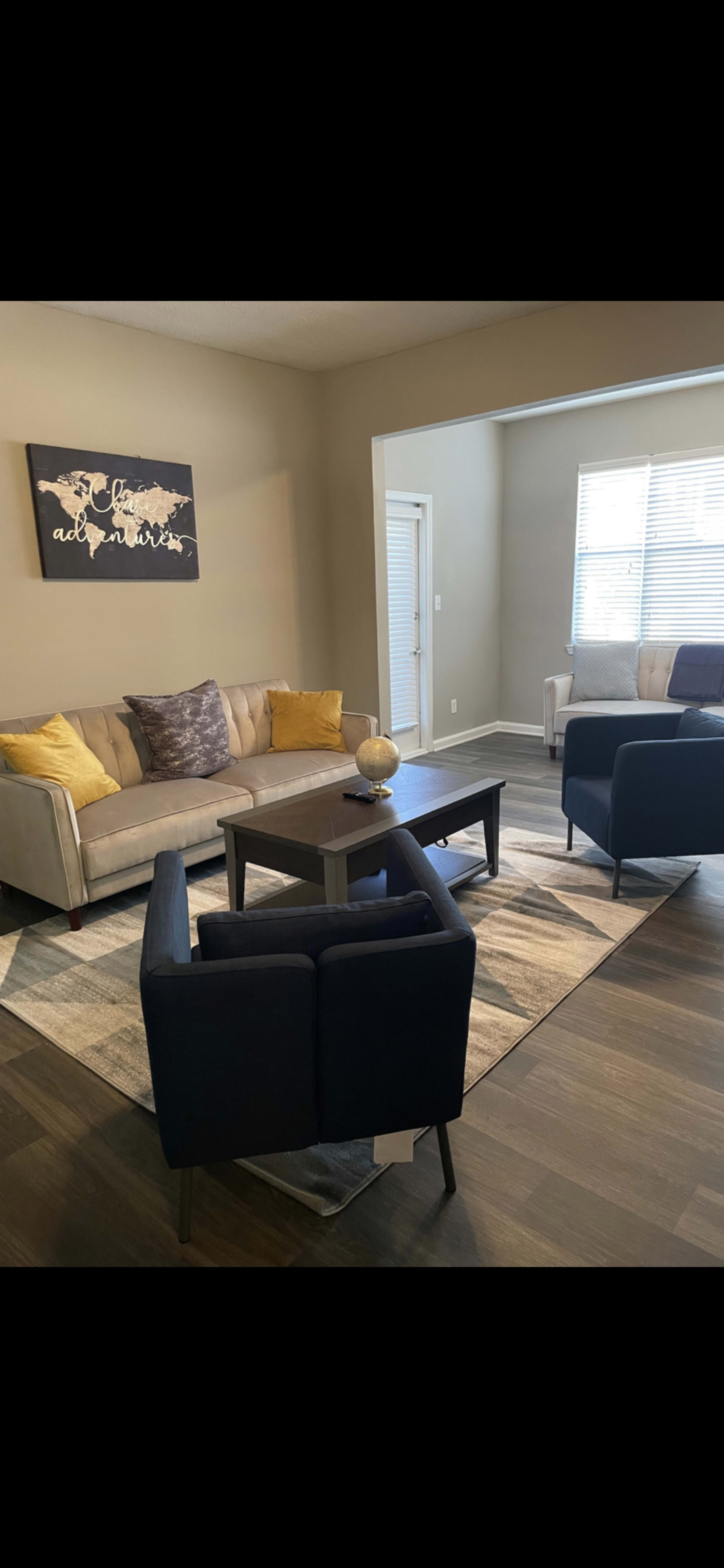 A living room with a grey sofa, two blue armchairs, a coffee table, and a decorative wall art piece.