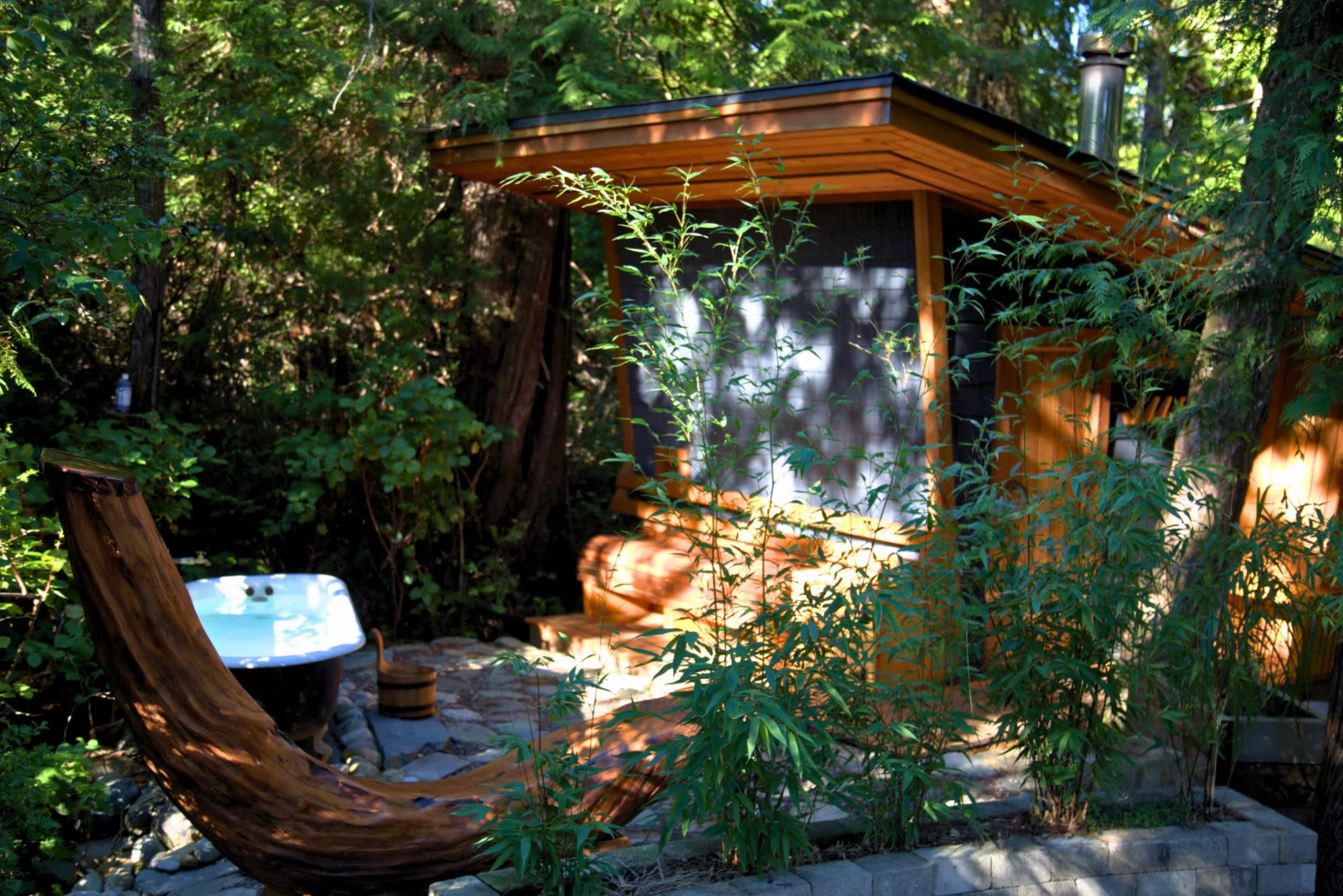 A wooden cabin surrounded by lush greenery and a freestanding bathtub sits in the garden.