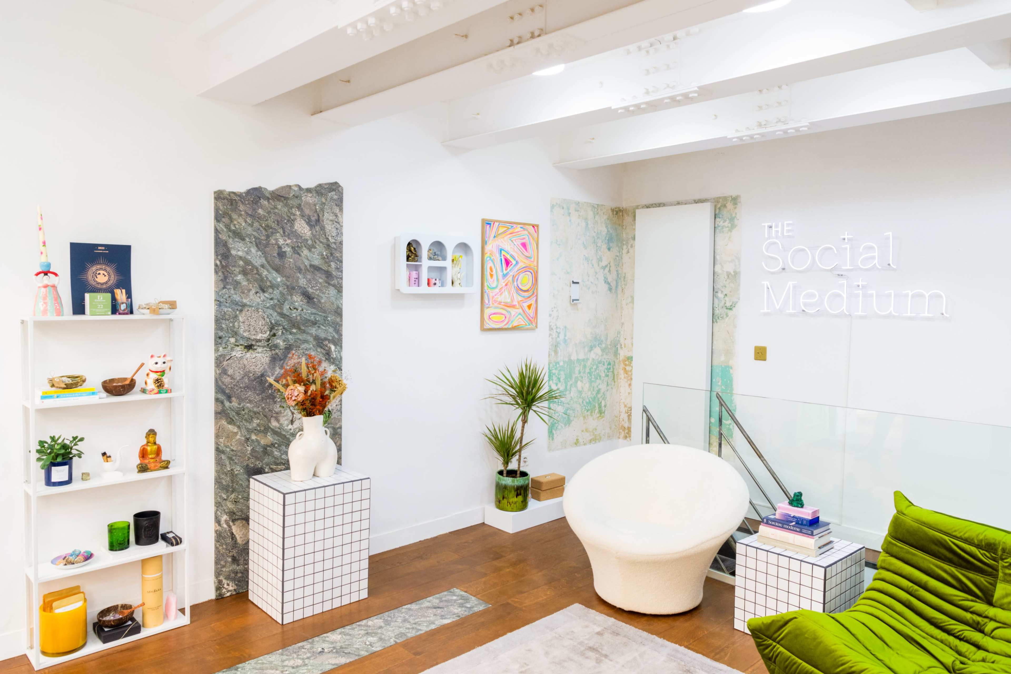 A modern interior space featuring a white armchair, a green sofa, decorative shelves, and colorful wall art.