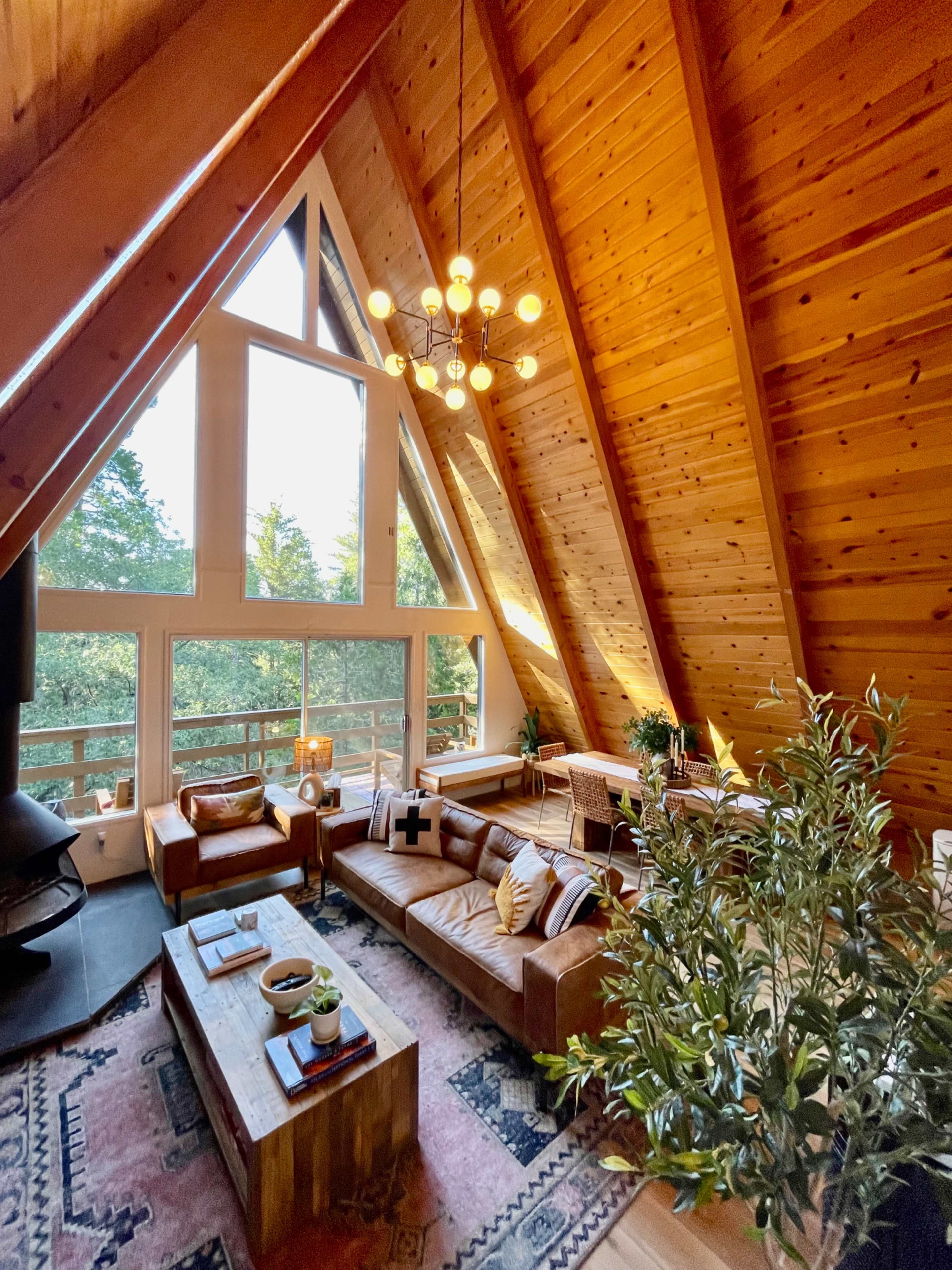 A spacious A-frame living room with wooden beams, large windows, and a comfortable seating area featuring a leather sofa and a coffee table.