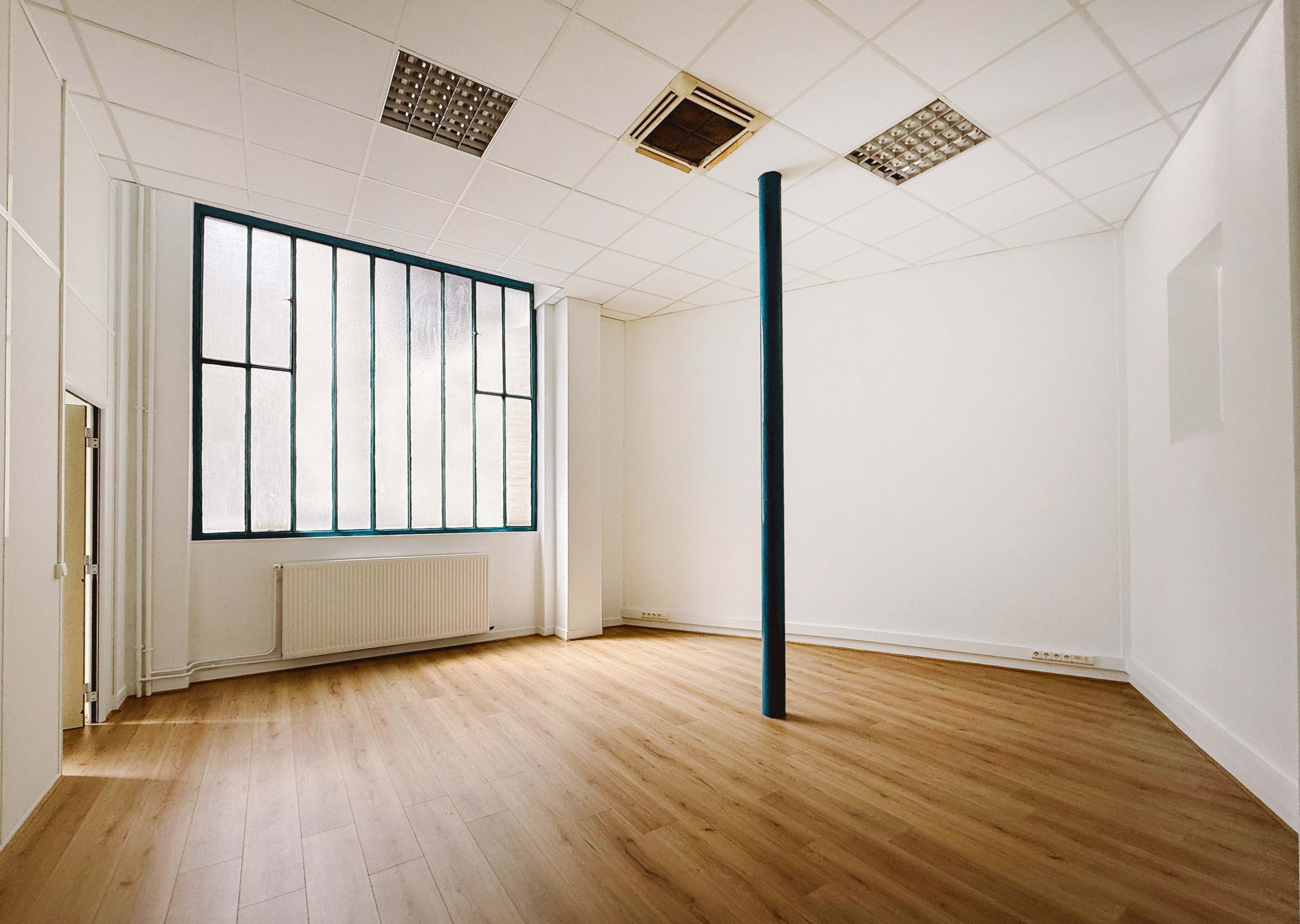 The image shows an empty room with wooden flooring, a large window with vertical panes, and a single blue vertical column in the center.