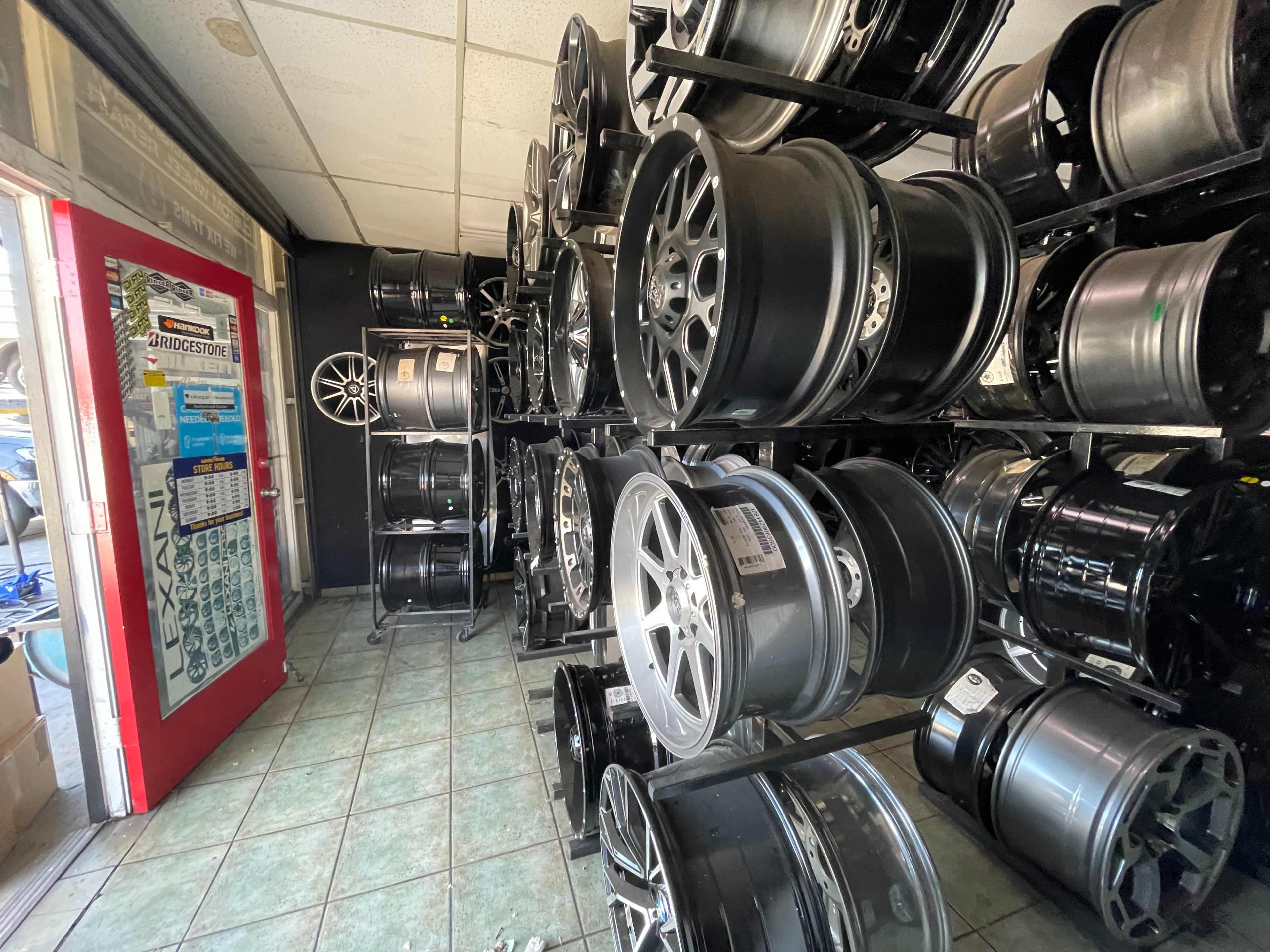 The image shows a narrow aisle in a shop lined with shelves displaying various car rims and wheels.
