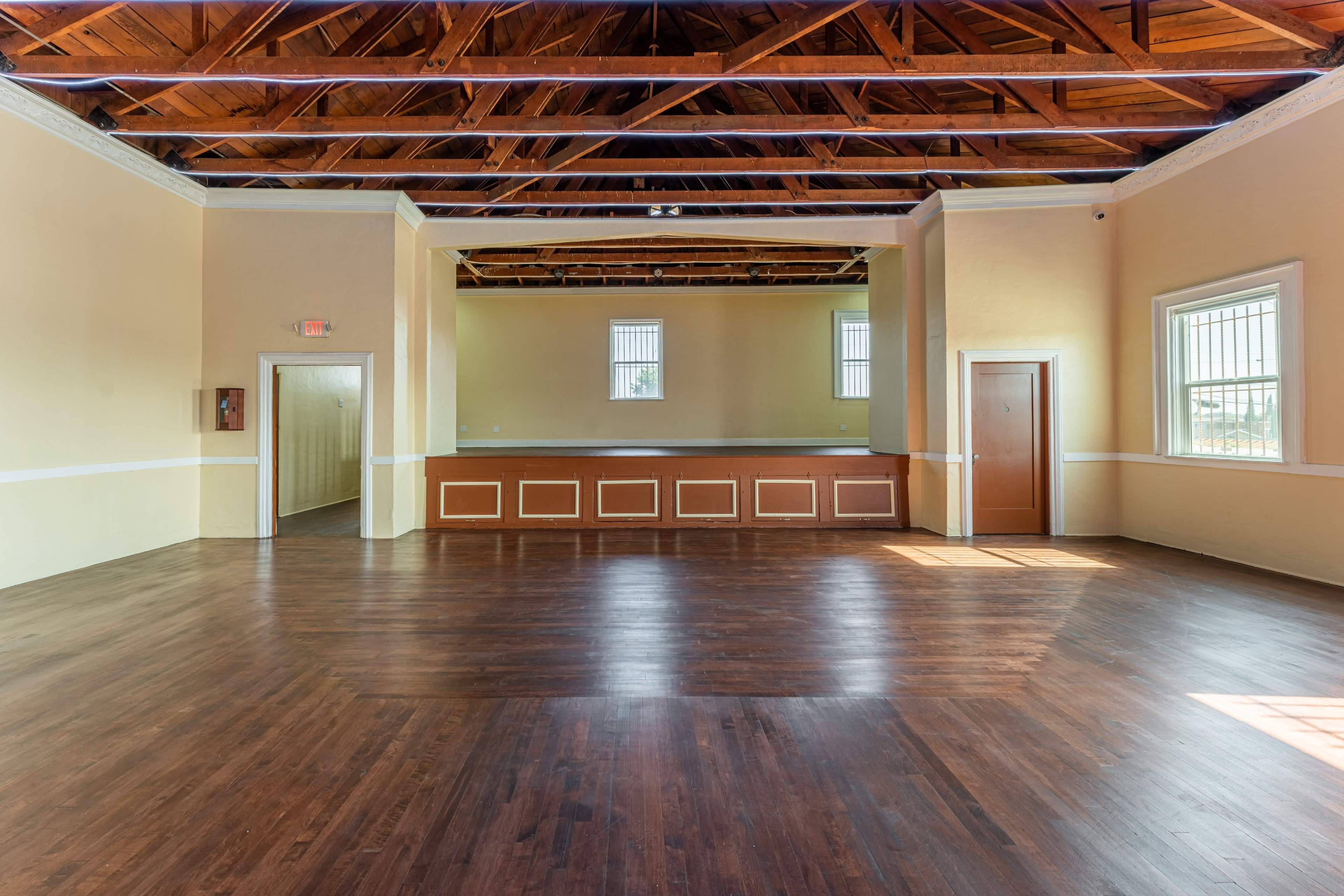 A spacious room with wooden floors, high ceilings, and a raised area at the back.