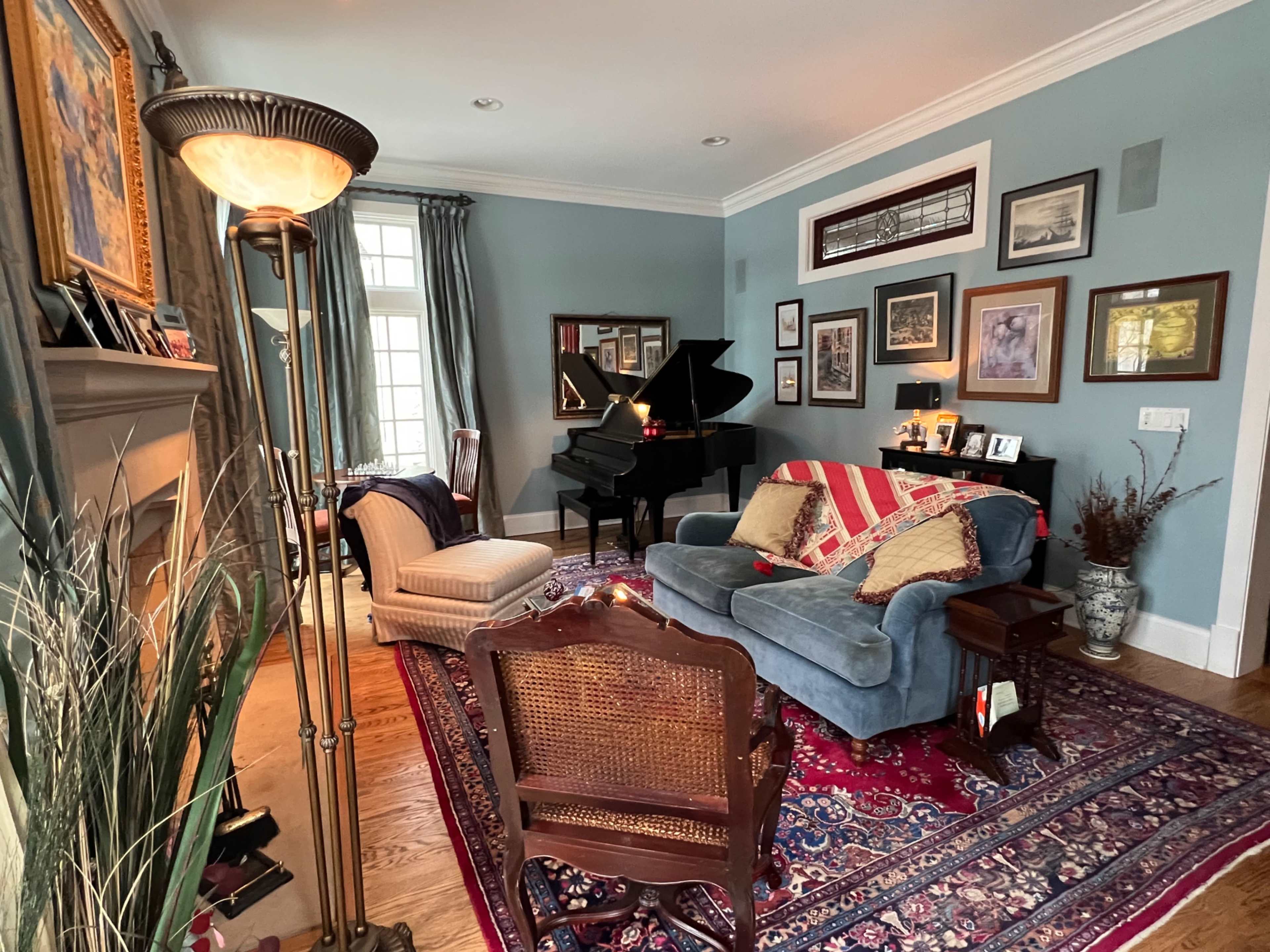 The image shows a cozy living room featuring a grand piano, a blue couch with striped pillows, and various framed artworks on the walls.