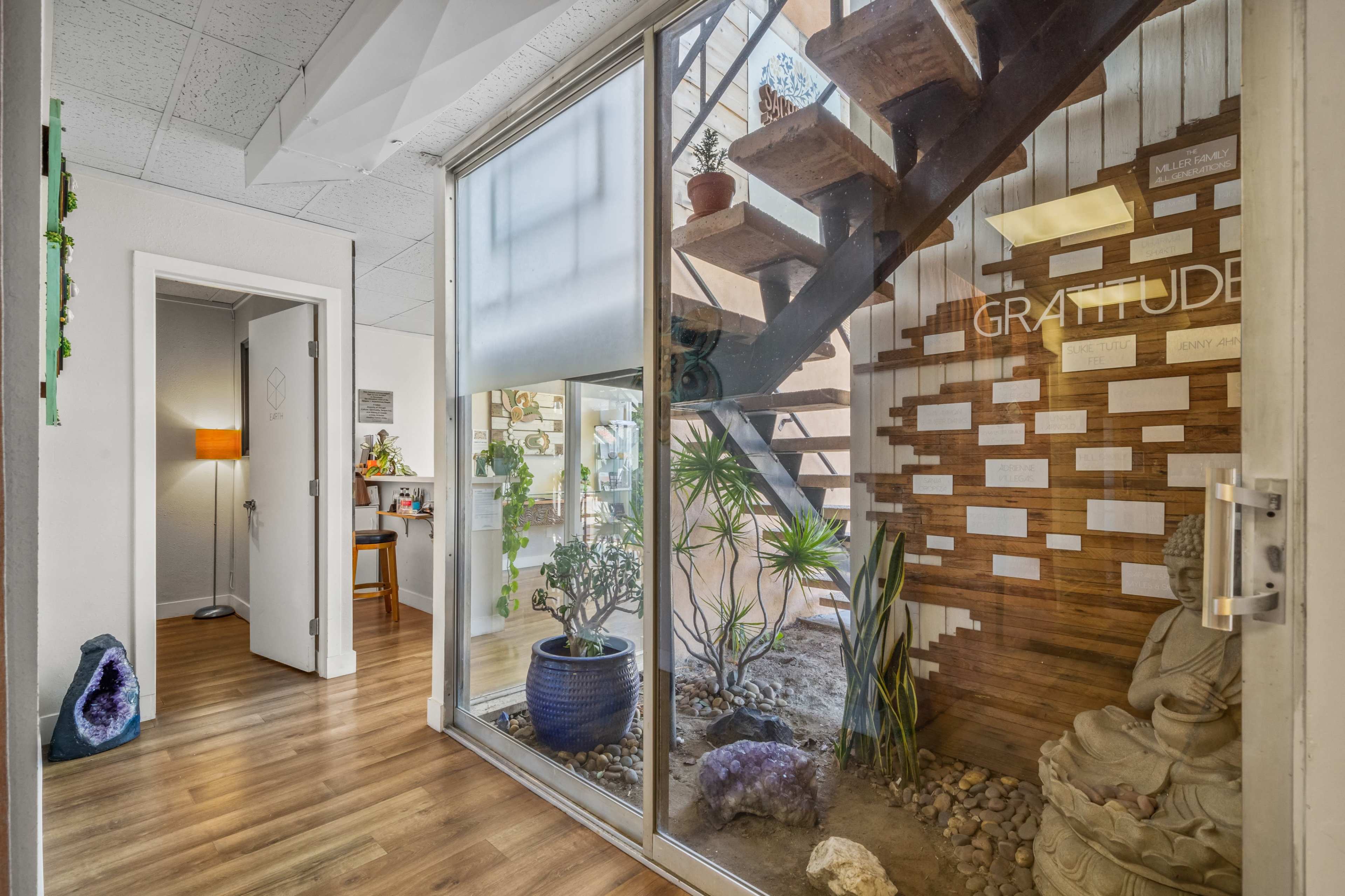 The image shows a modern indoor space featuring a staircase, plants, a wall with wooden paneling, and a statue in a well-lit corridor.