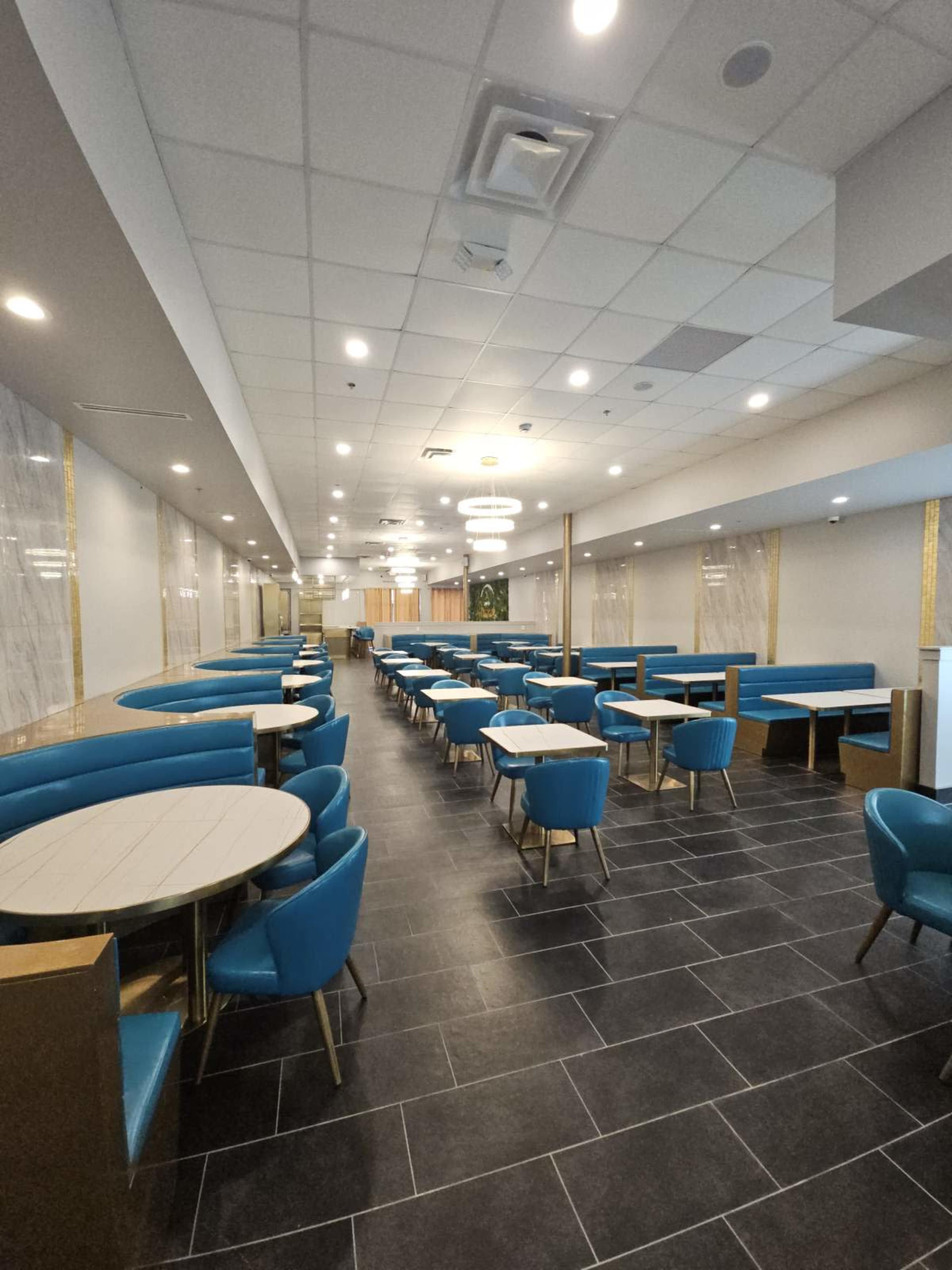 The image shows a spacious restaurant interior featuring blue seating, round tables, and modern decor, with a tiled floor and ambient lighting.
