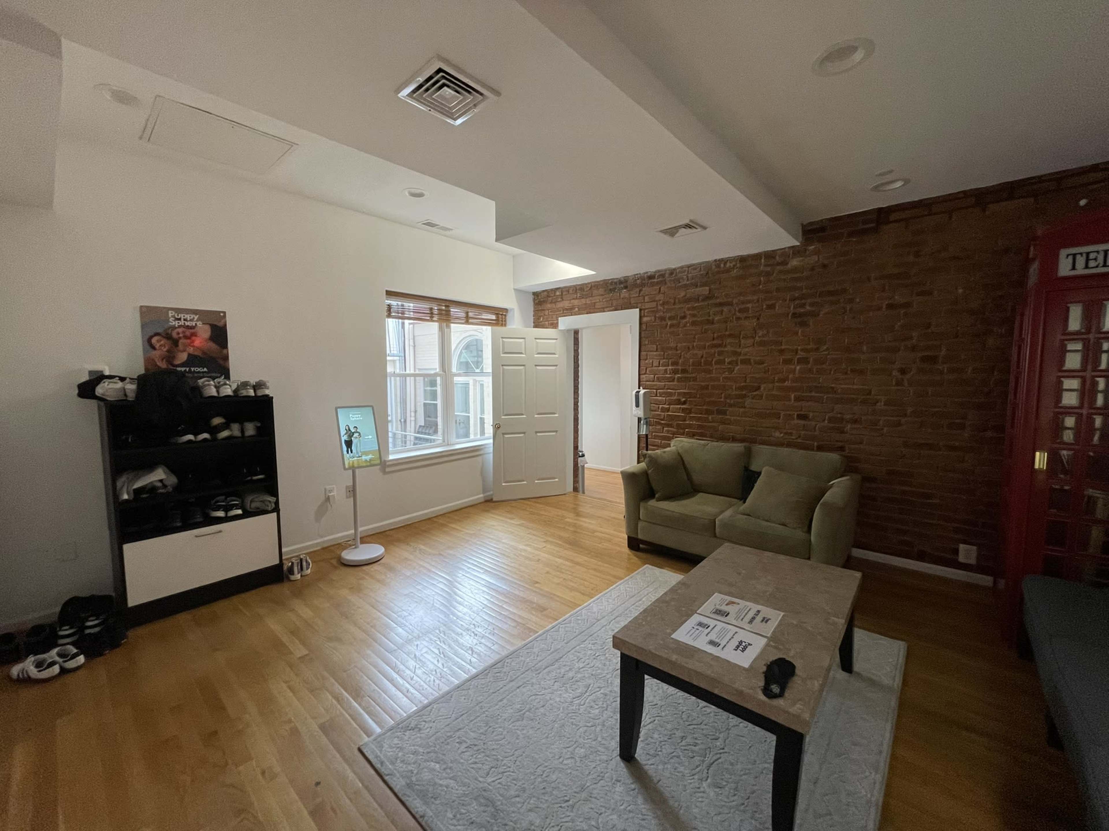 The room features a mix of exposed brick and white walls, furnished with a green couch, a coffee table, and a shelf displaying shoes.