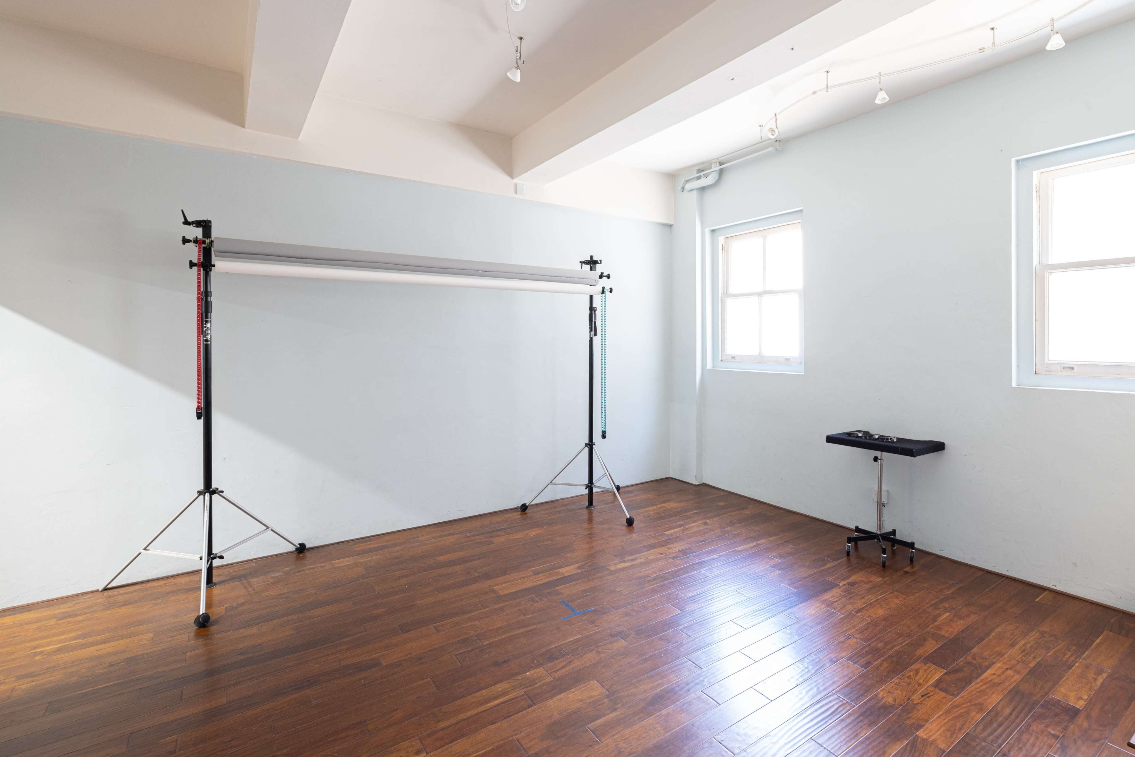 The image shows a vacant room with wooden flooring, featuring two light stands supporting a backdrop, and a small table against one wall.