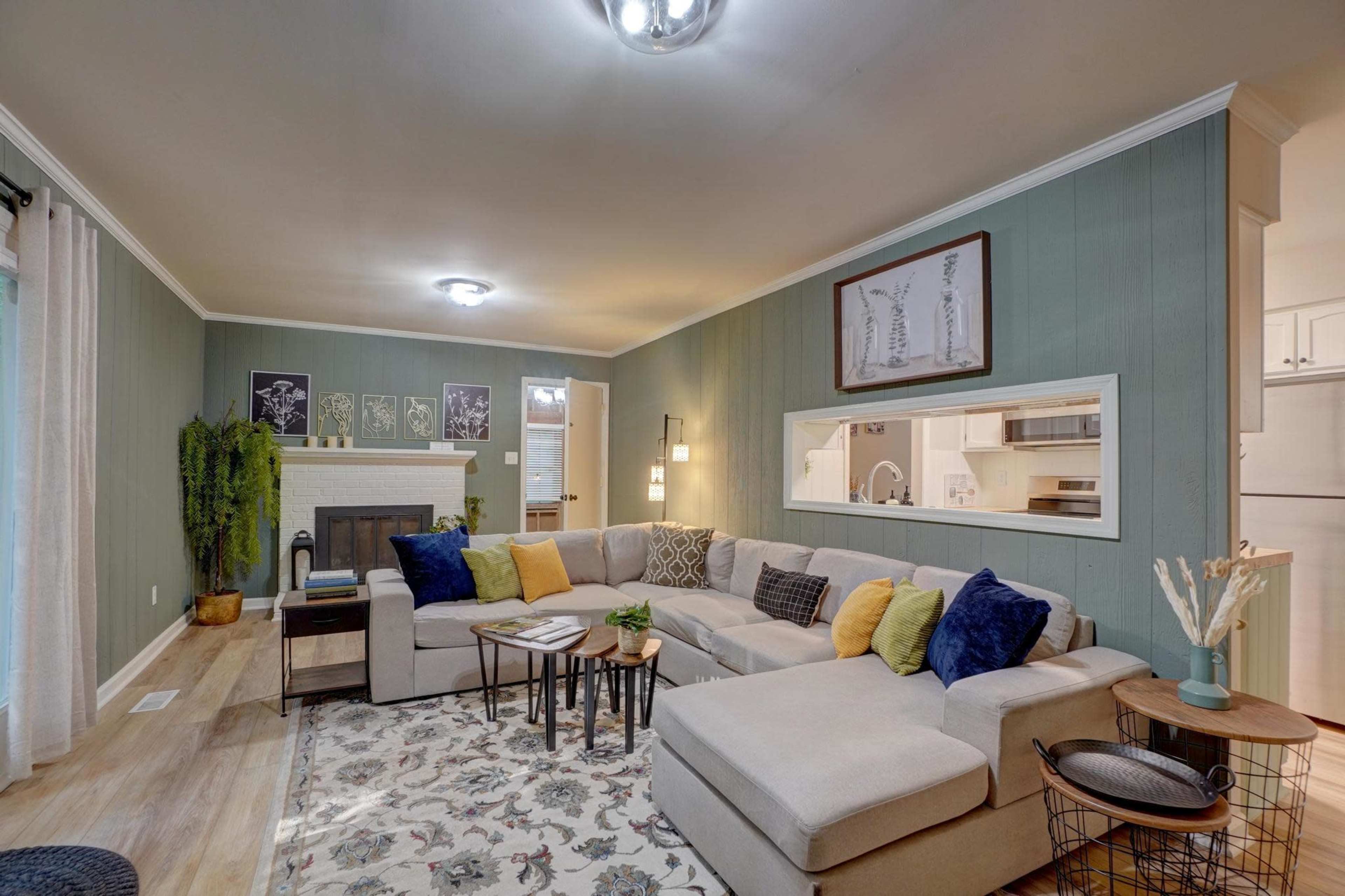 The living room features a sectional sofa, a coffee table, and a decorative area rug, with green wall paneling and a fireplace as central elements.