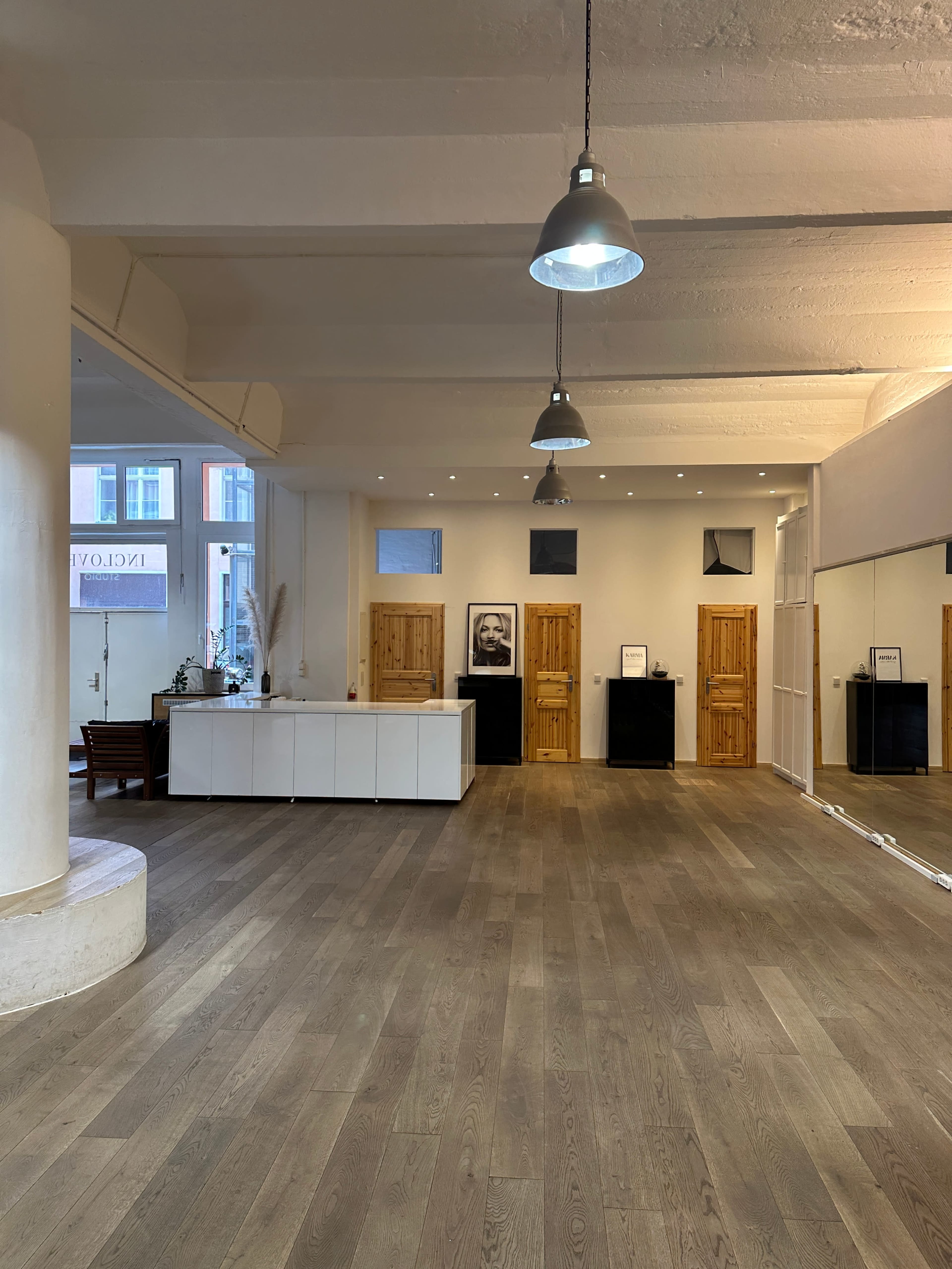 The image shows a spacious interior with wooden flooring, a white reception desk, and wooden doors lined along the walls.
