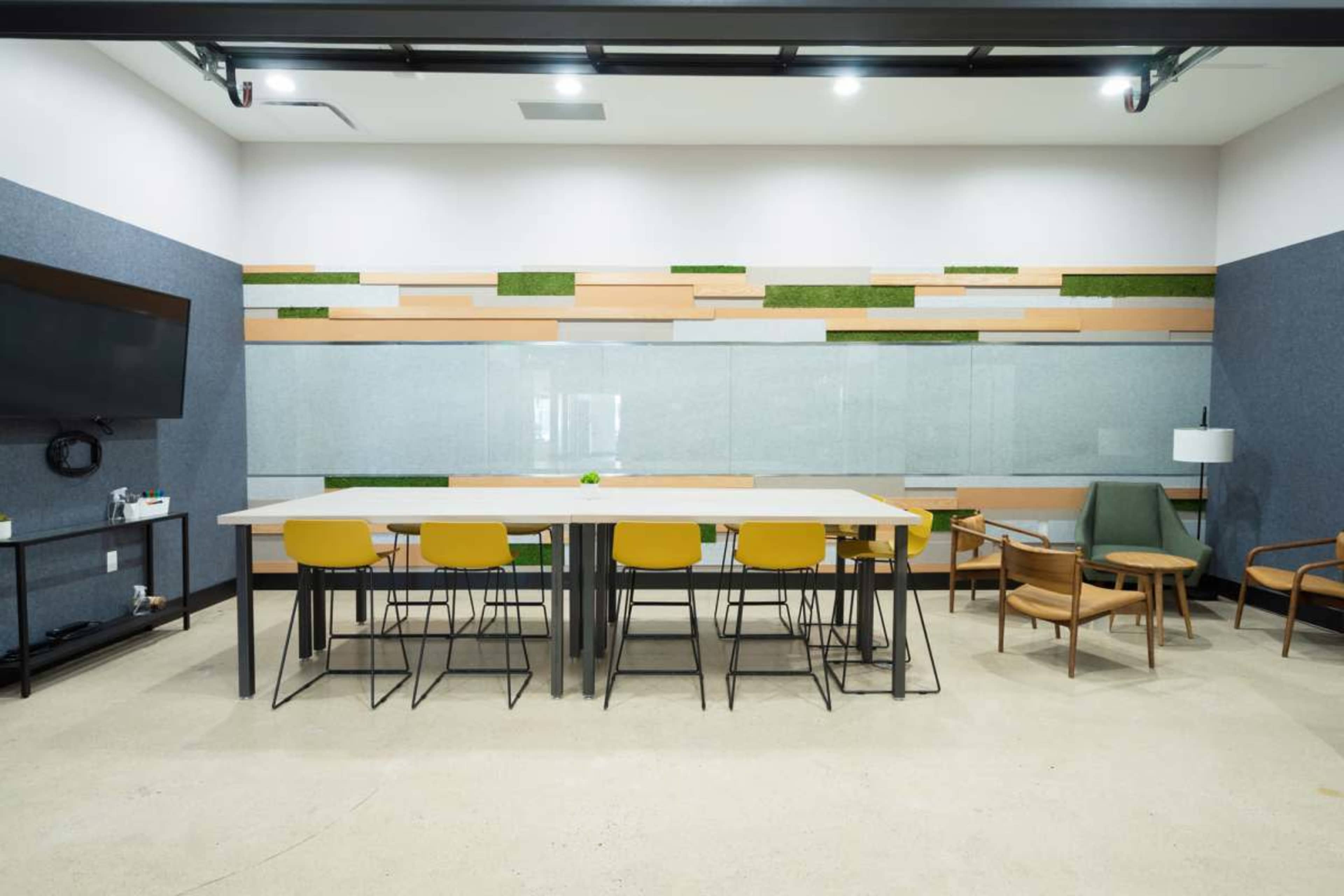 The image shows a modern conference room with a long table, yellow chairs, a large glass wall, and decorative wall elements featuring greenery.