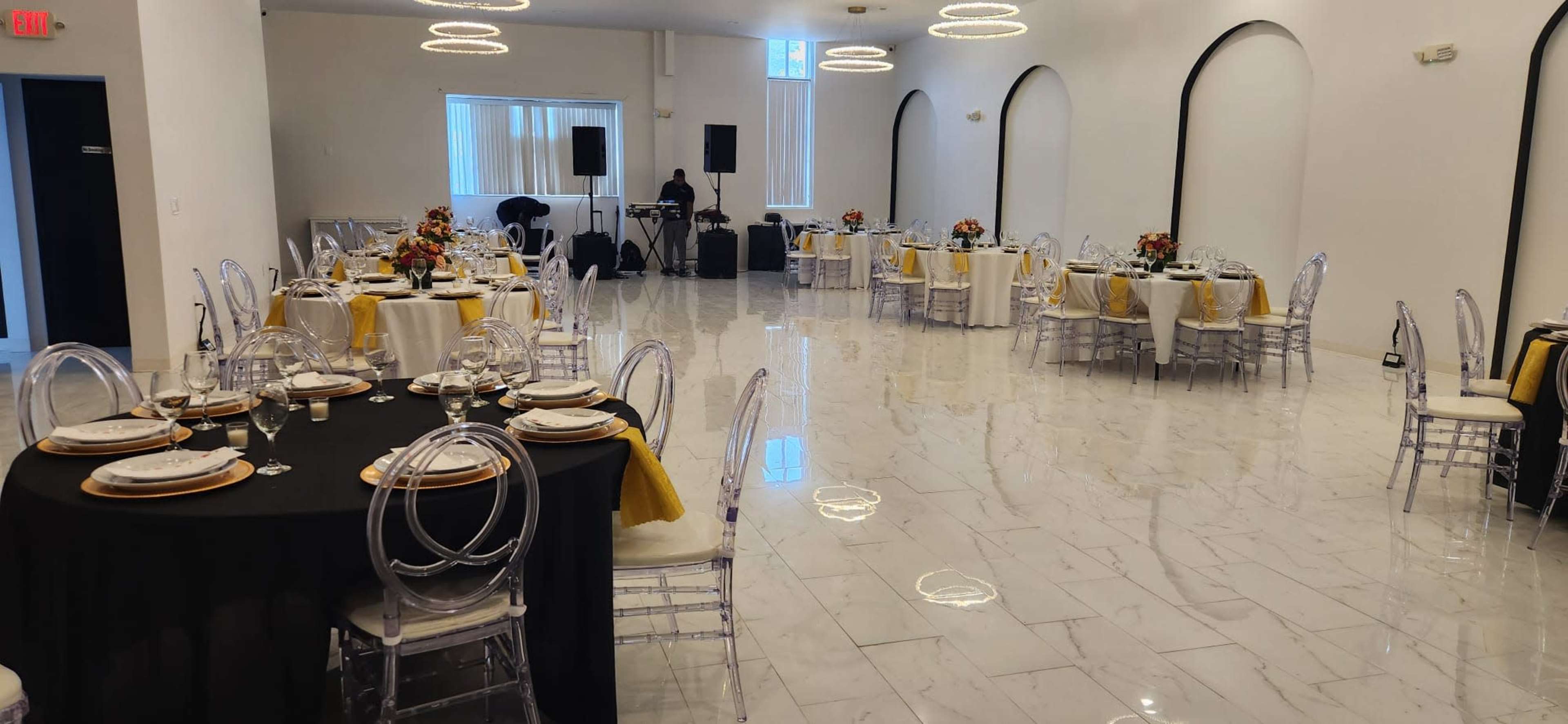A spacious event hall set with round tables dressed in black and gold tablecloths, arranged for a formal gathering.