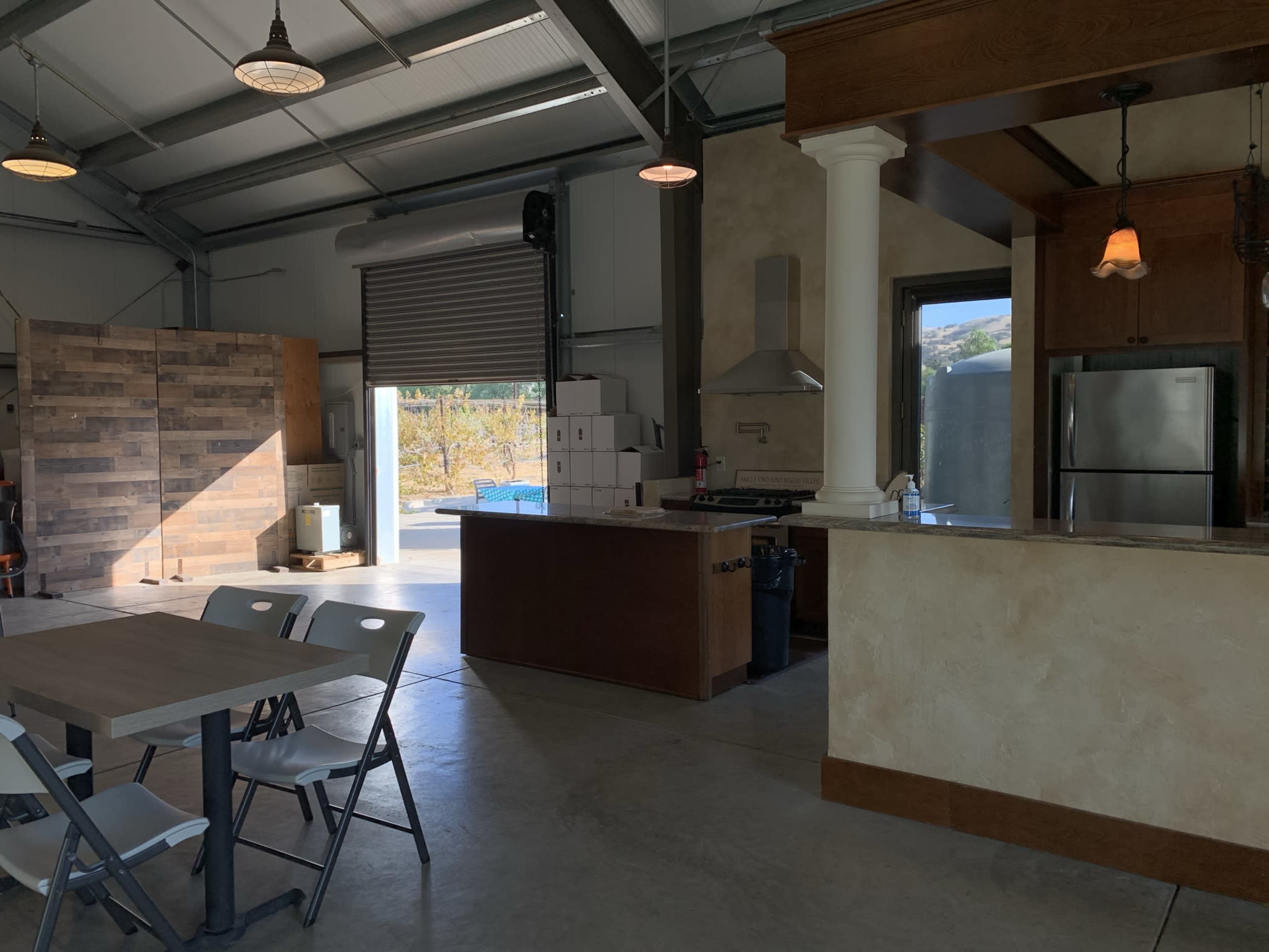 A spacious interior of a building featuring a kitchen area, a dining table with chairs, and a wall made of wooden panels.