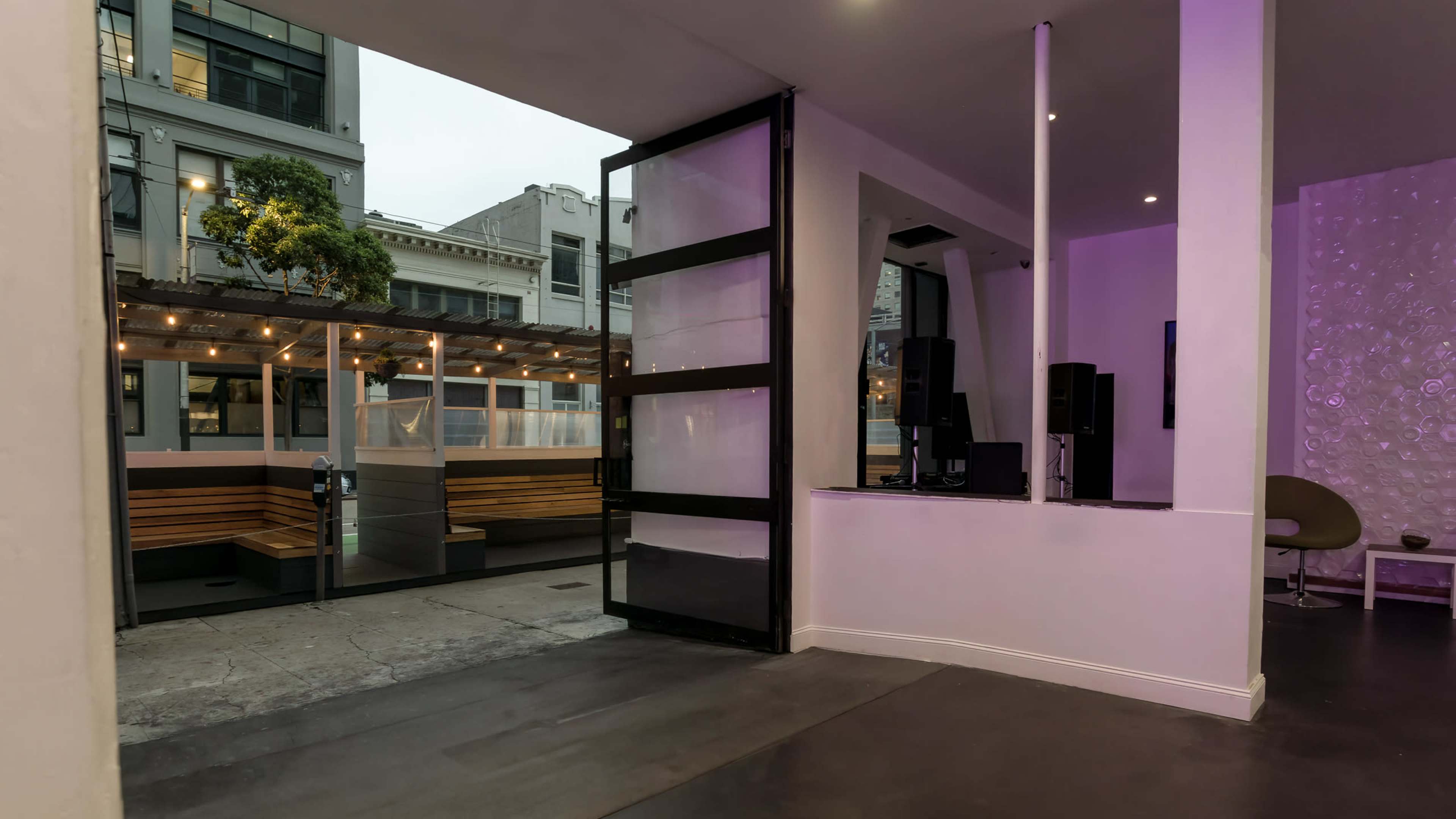 A modern indoor space with large glass doors leading to an outdoor seating area illuminated by string lights.