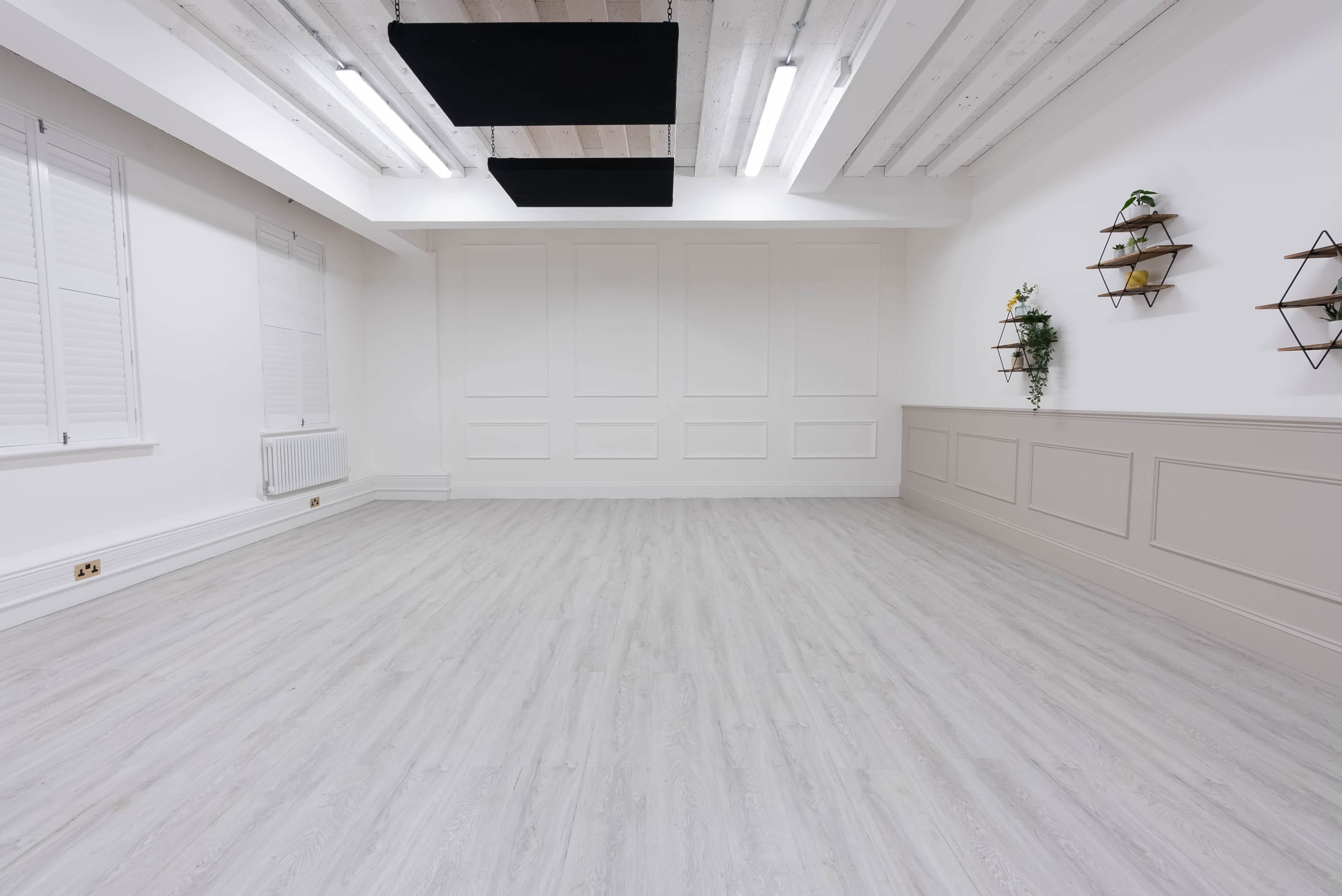 A spacious, empty room with light-colored walls, wooden flooring, and decorative wall shelves.