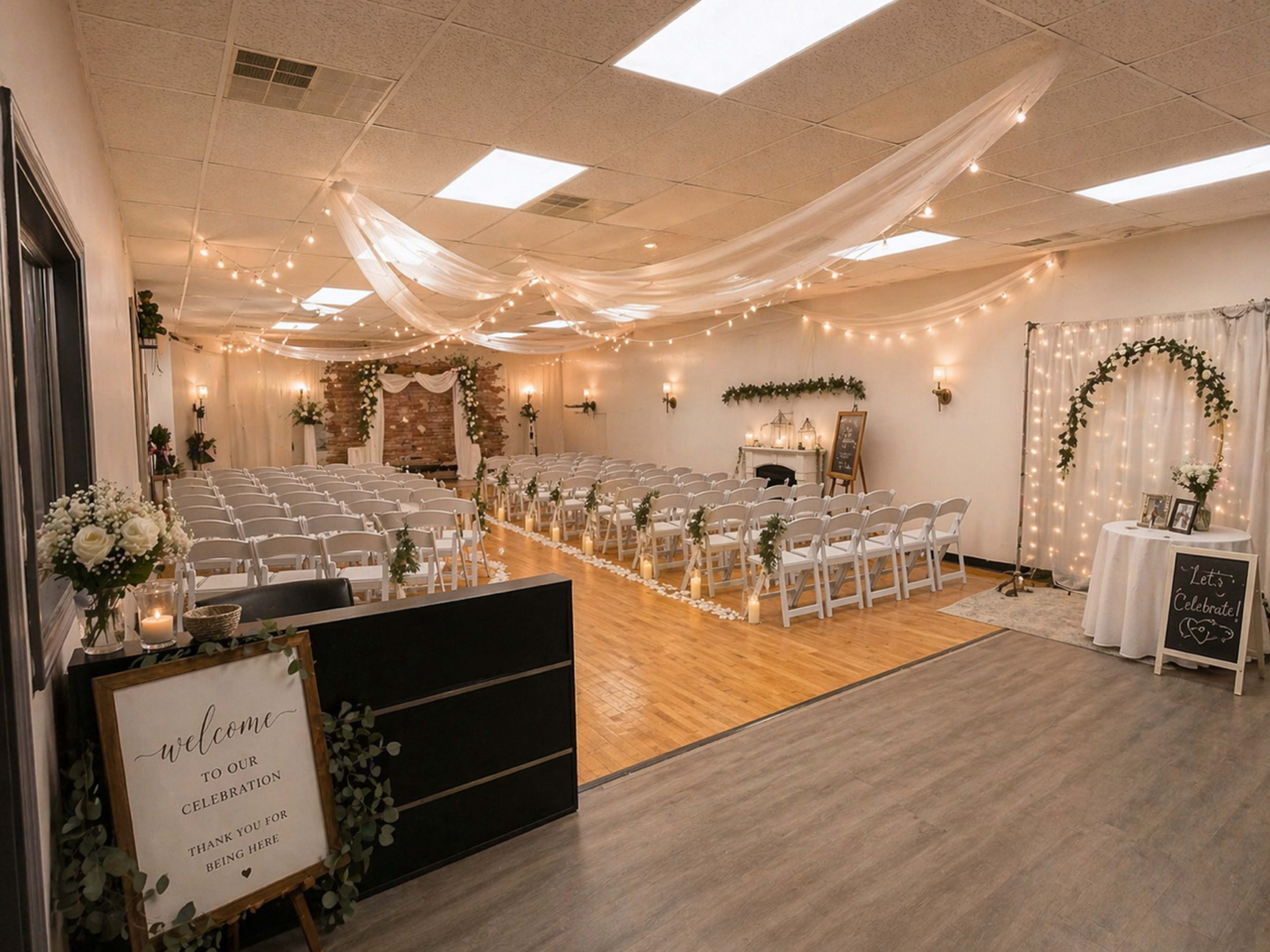 The image shows a decorated indoor venue for a celebration, featuring rows of white chairs, string lights, and floral arrangements.