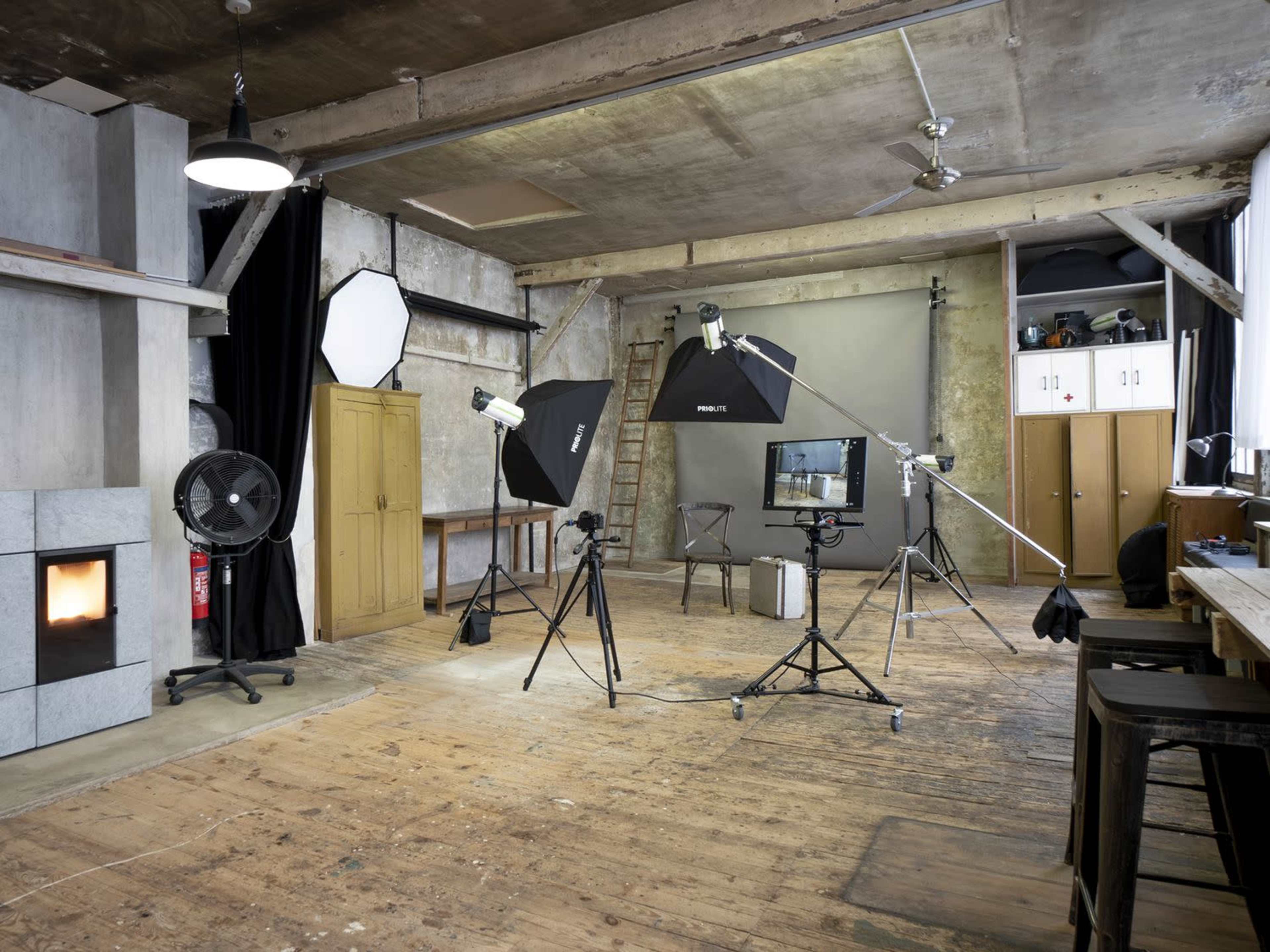 A photography studio features multiple lighting setups, a backdrop, and wooden flooring, with equipment strategically arranged around the space.