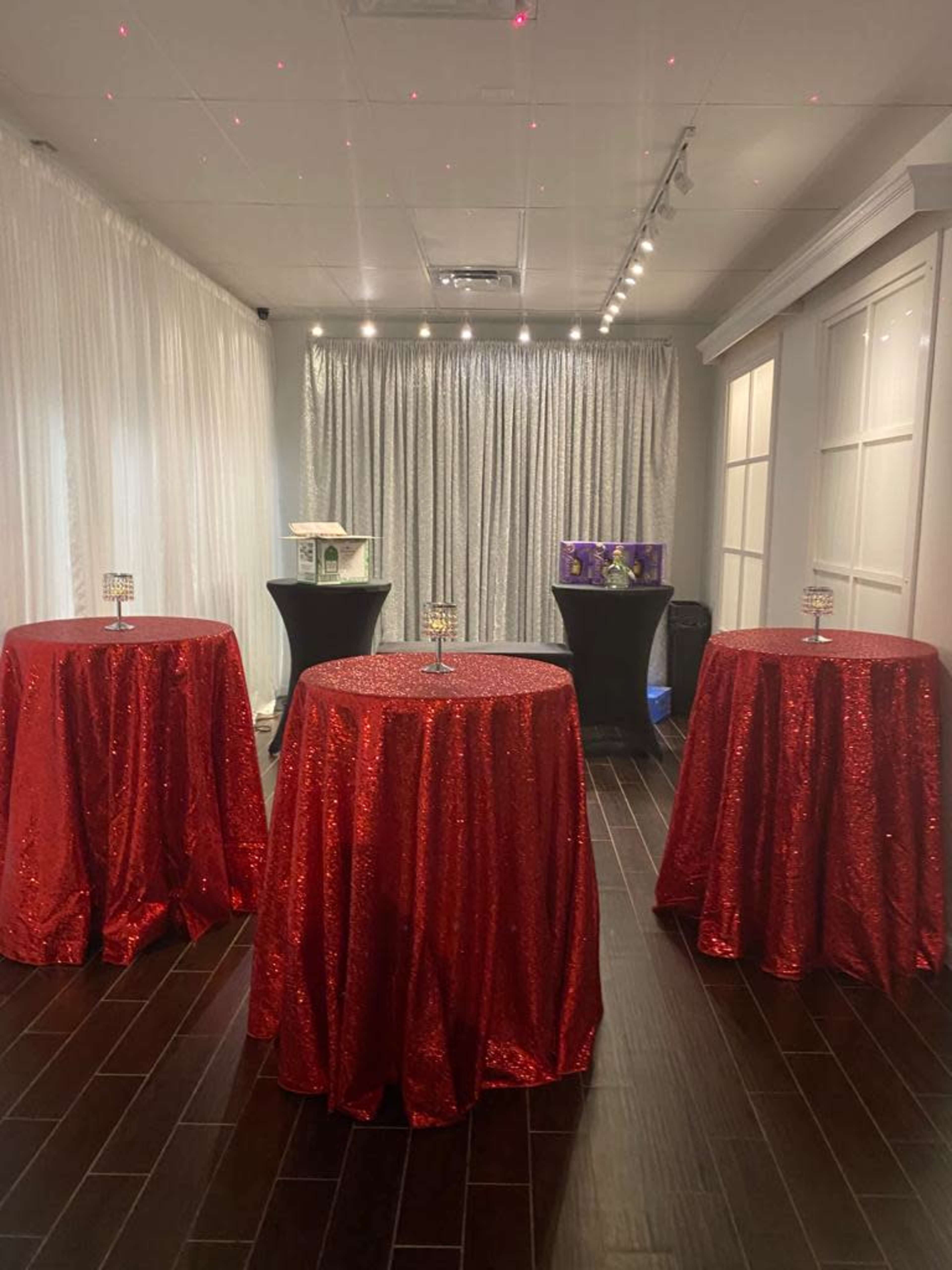 The image shows a room decorated with four red sequin tablecloths on tall round tables, with a backdrop of silver drapery and dim lighting.