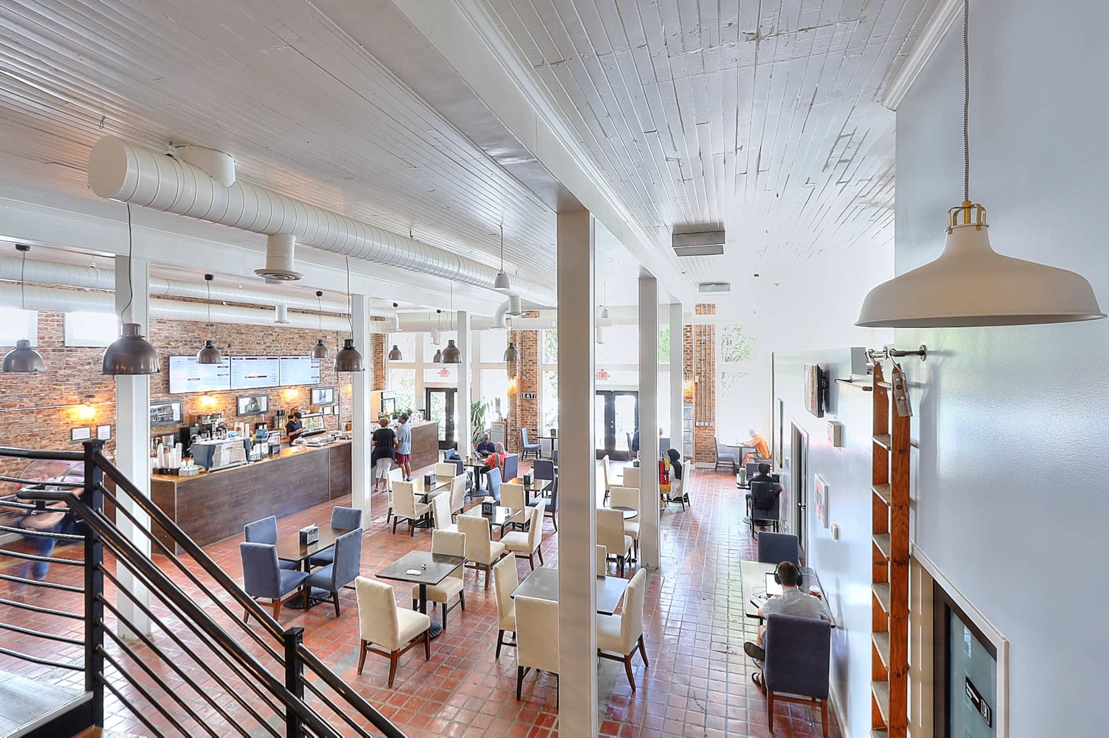 A spacious café with a modern design, featuring a counter at the back and tables arranged throughout the area.