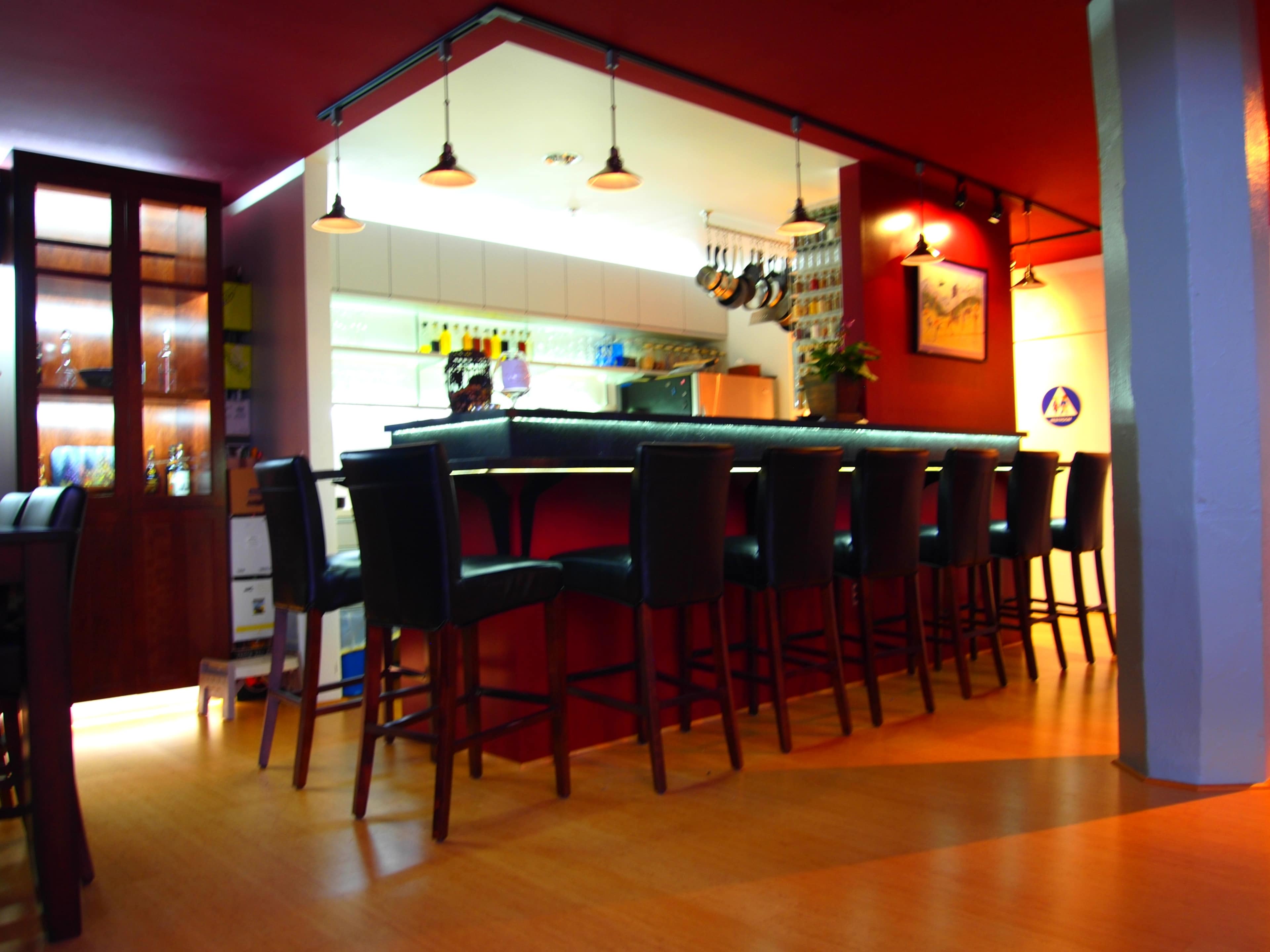 A well-lit bar area with high stools arranged around a dark countertop, set in a restaurant with a modern design.