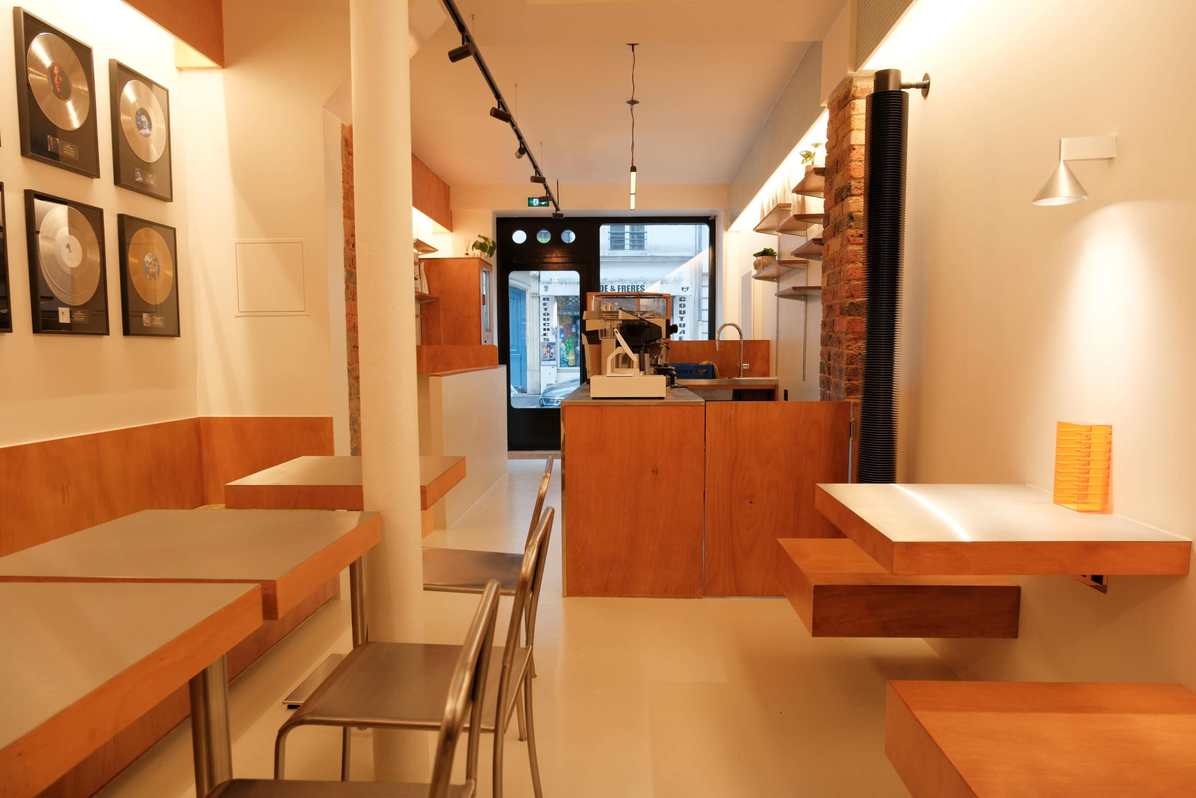The image shows the interior of a modern café with wooden furniture, a counter at the rear, and framed circular plaques on the walls.
