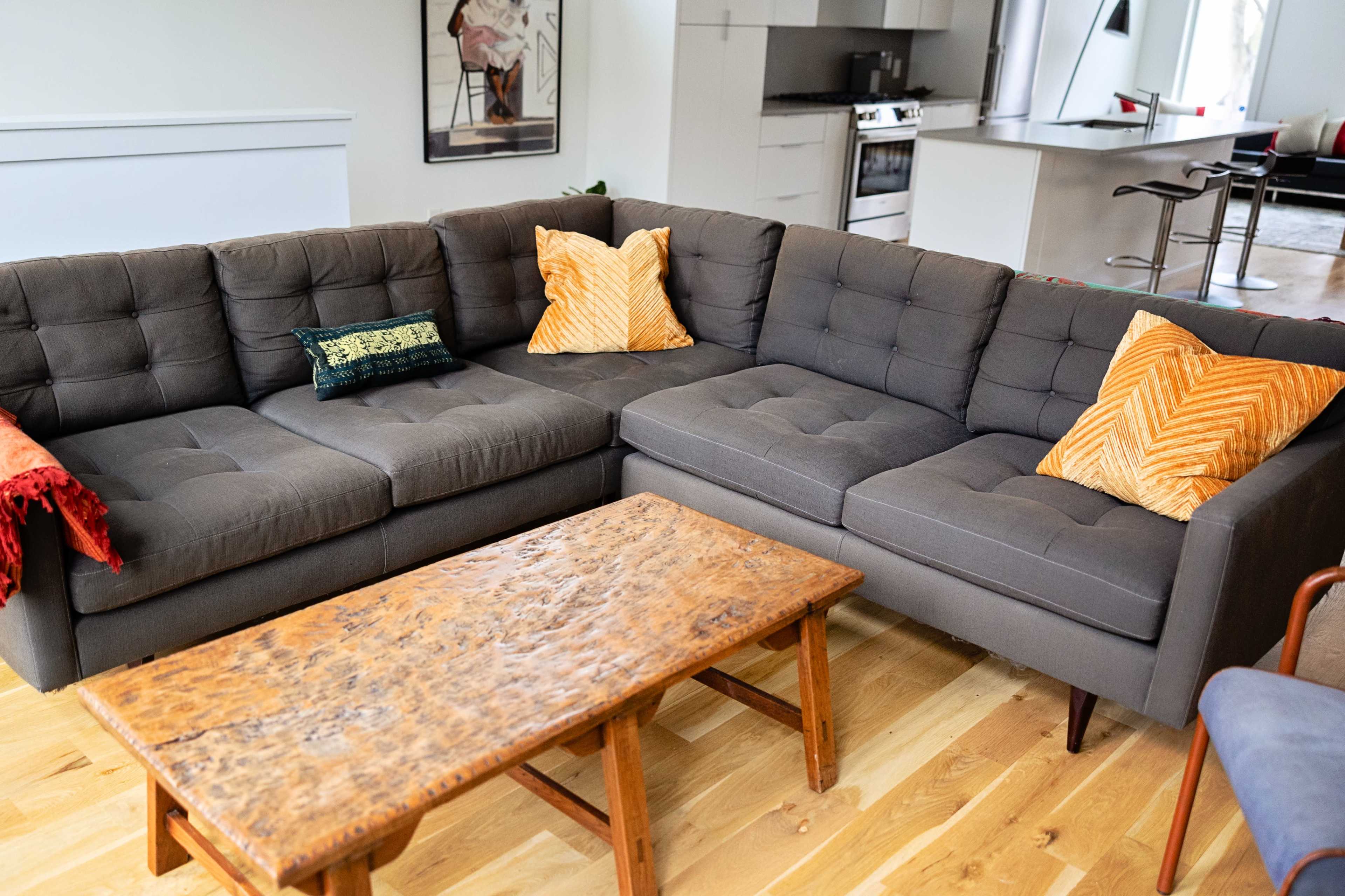 A gray sectional sofa with two patterned throw pillows is positioned next to a wooden coffee table on a hardwood floor.