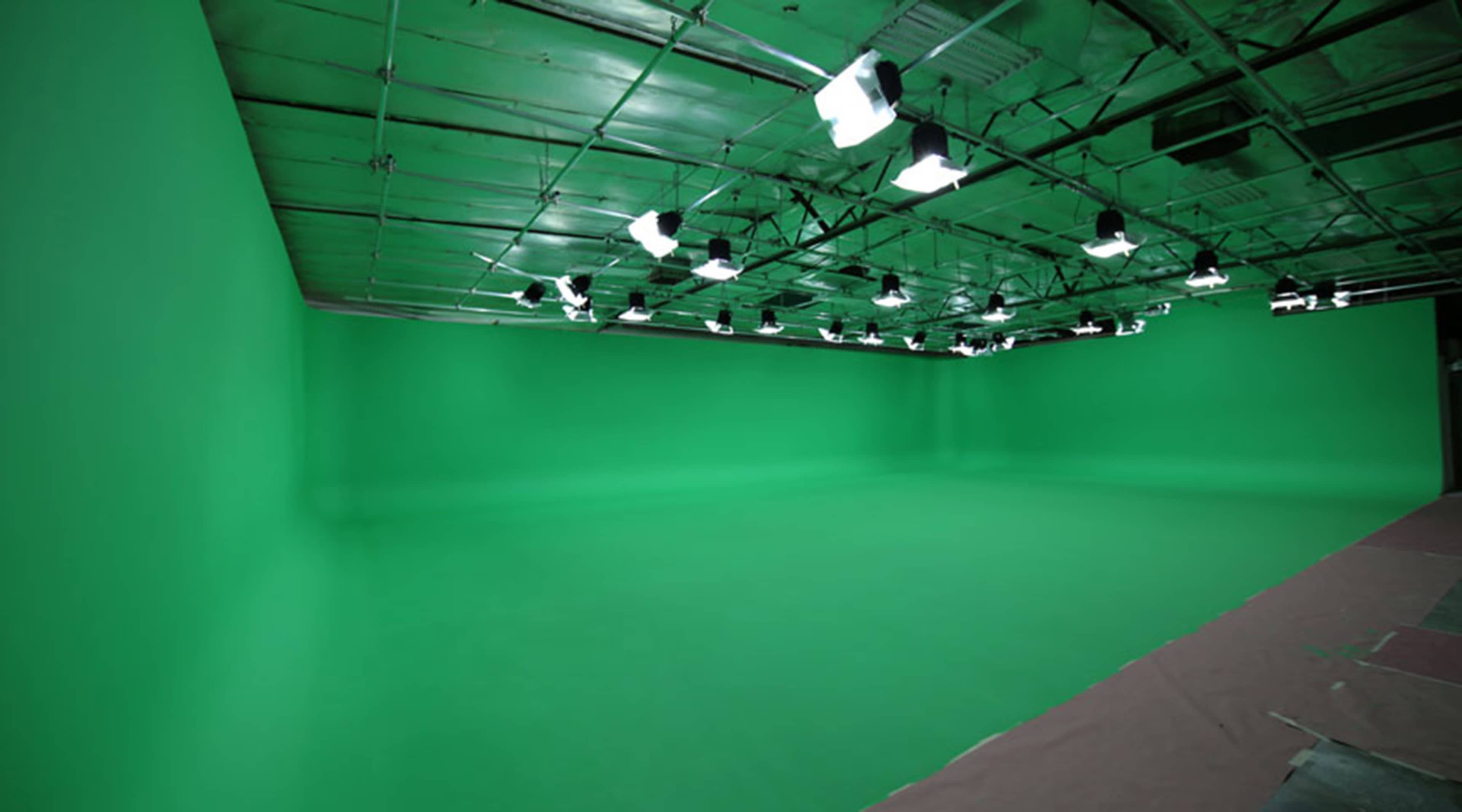A spacious studio with a green screen backdrop and overhead lighting.