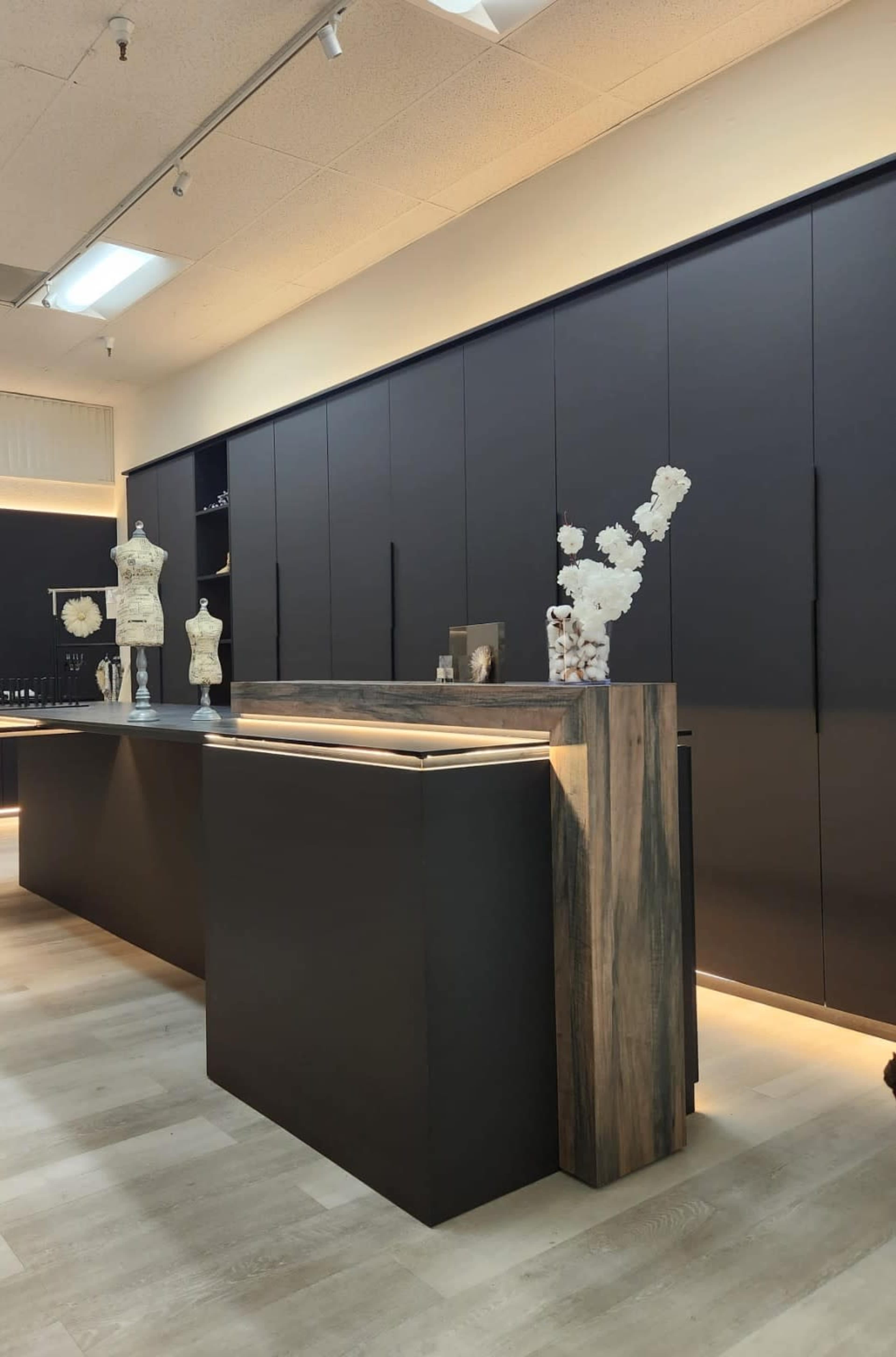 The image shows a modern retail space with a black reception counter, wooden accents, and display mannequins, illuminated by soft lighting.