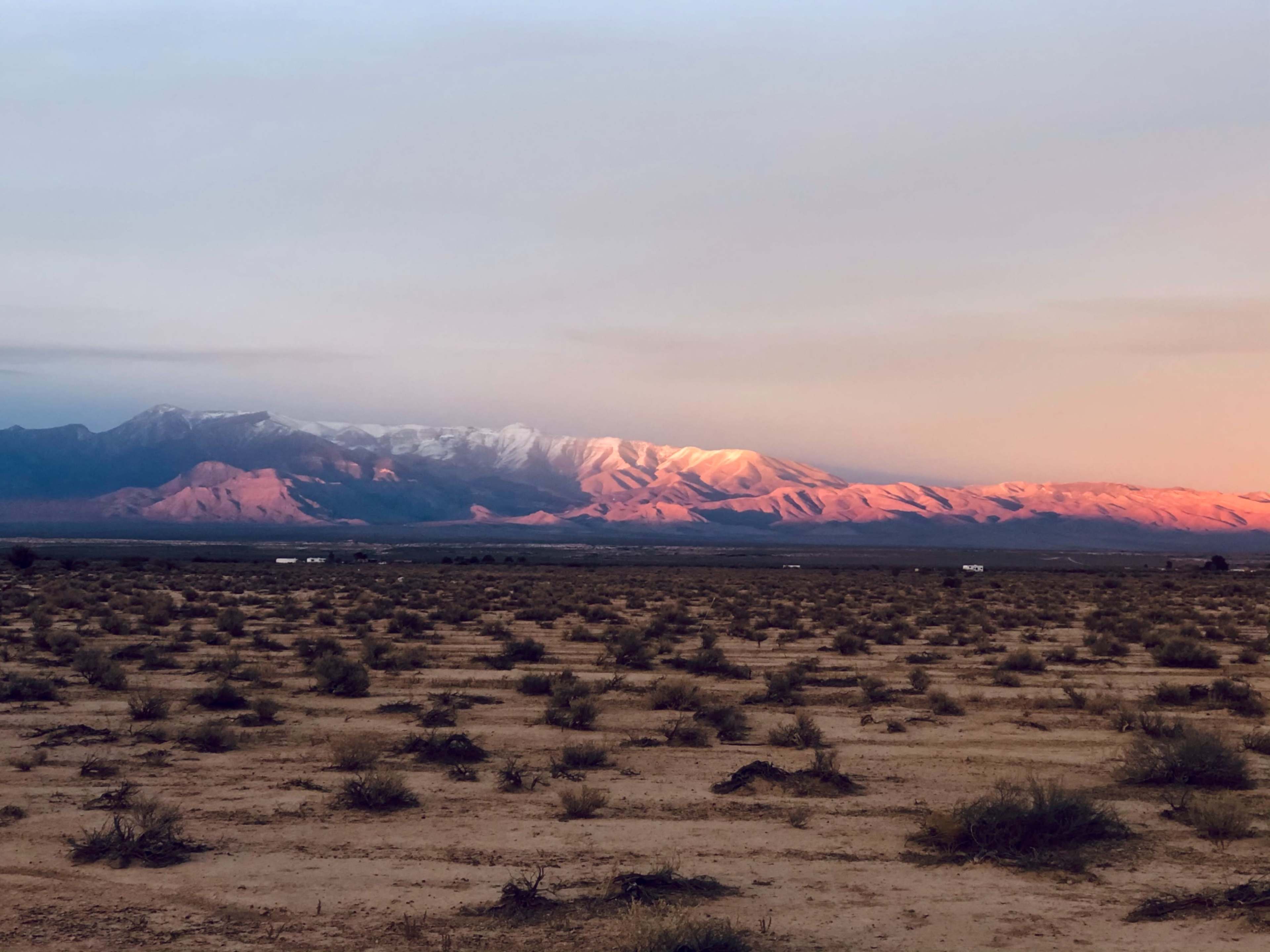 A barren landscape features a range of mountains bathed in warm light, with sparse vegetation scattered across the arid land.
