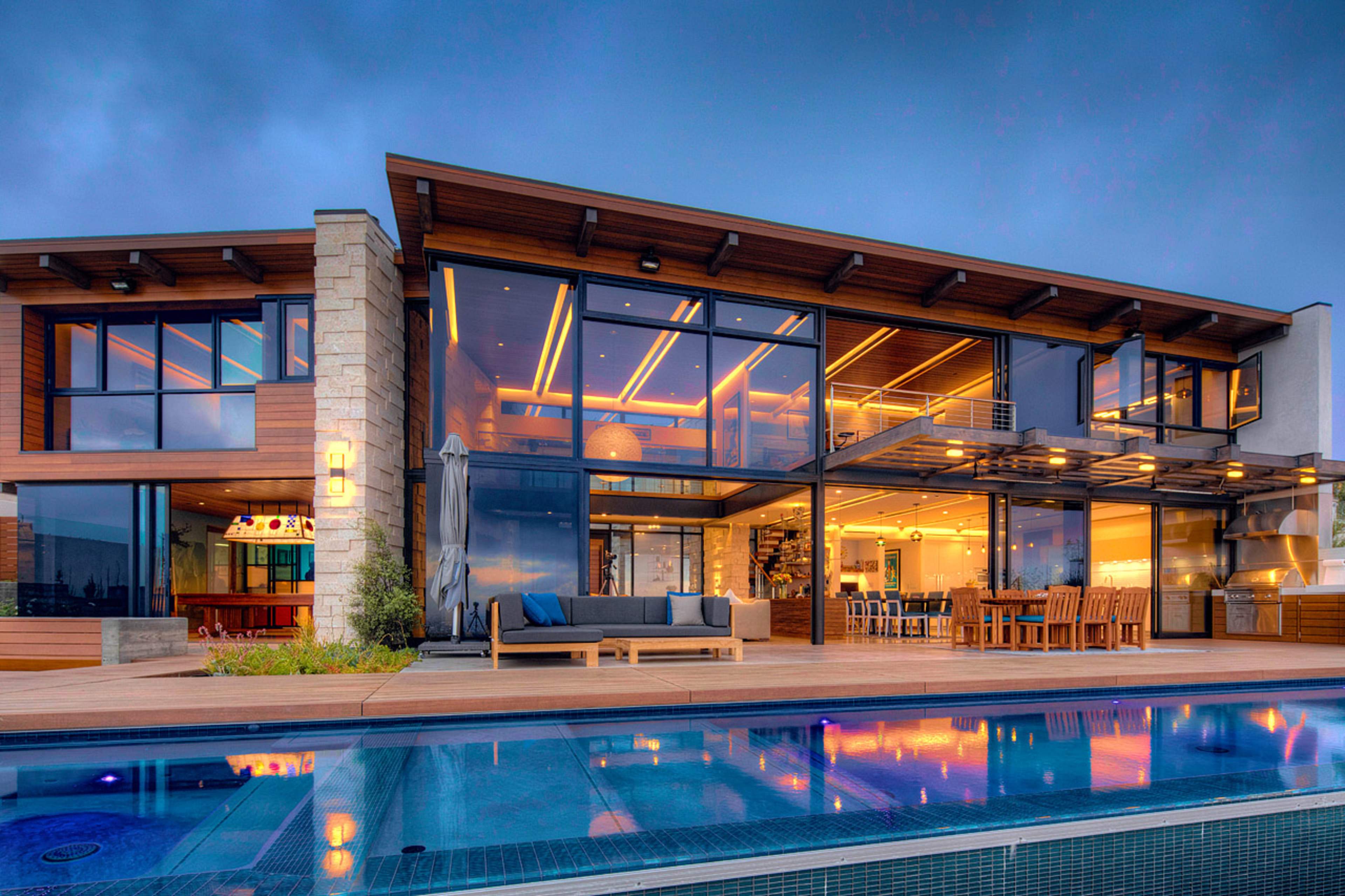 A modern two-story house features large glass windows and a patio by a swimming pool.