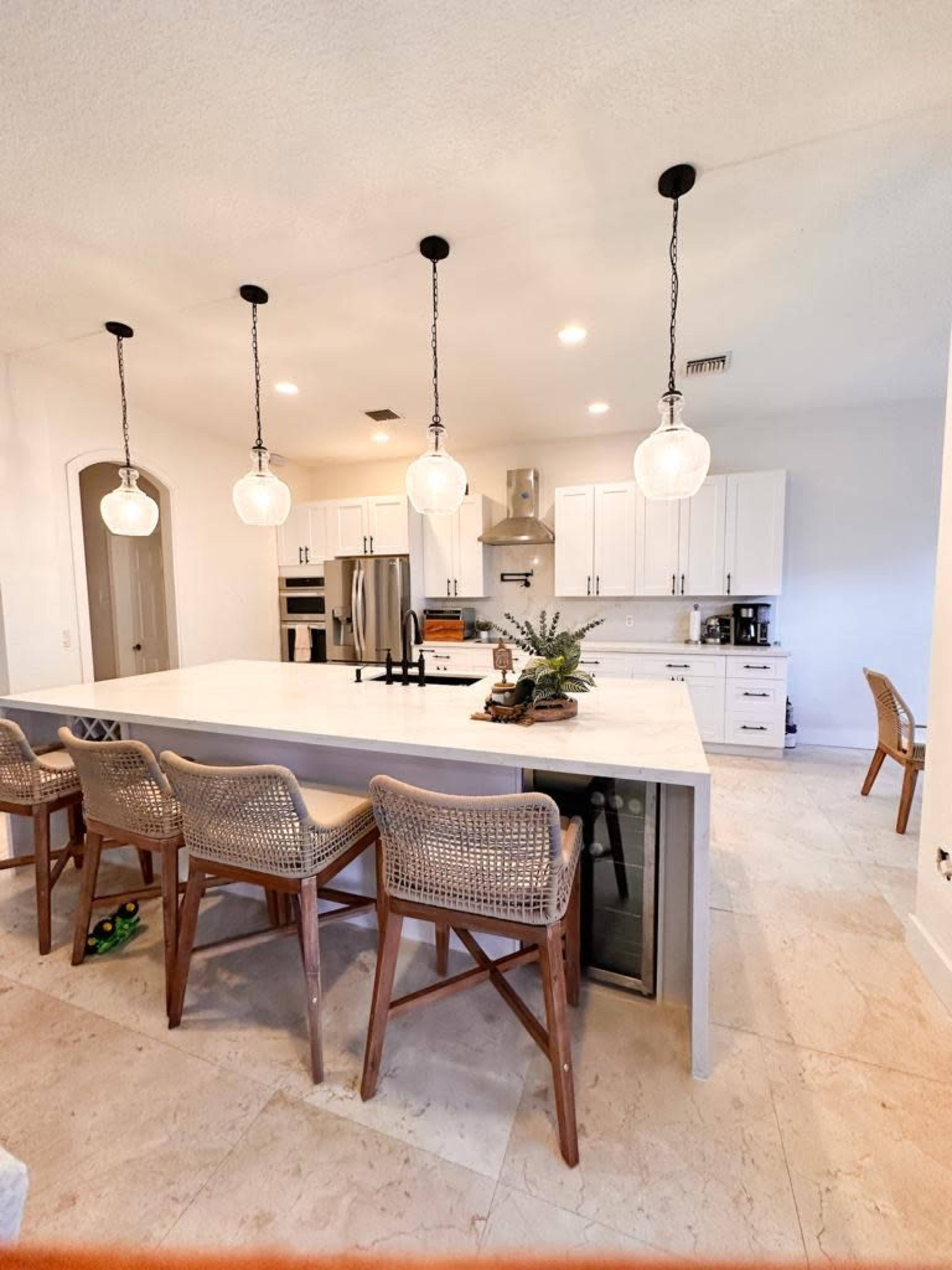 The image shows a modern kitchen with a large island featuring bar seating, pendant lights, and stainless steel appliances.