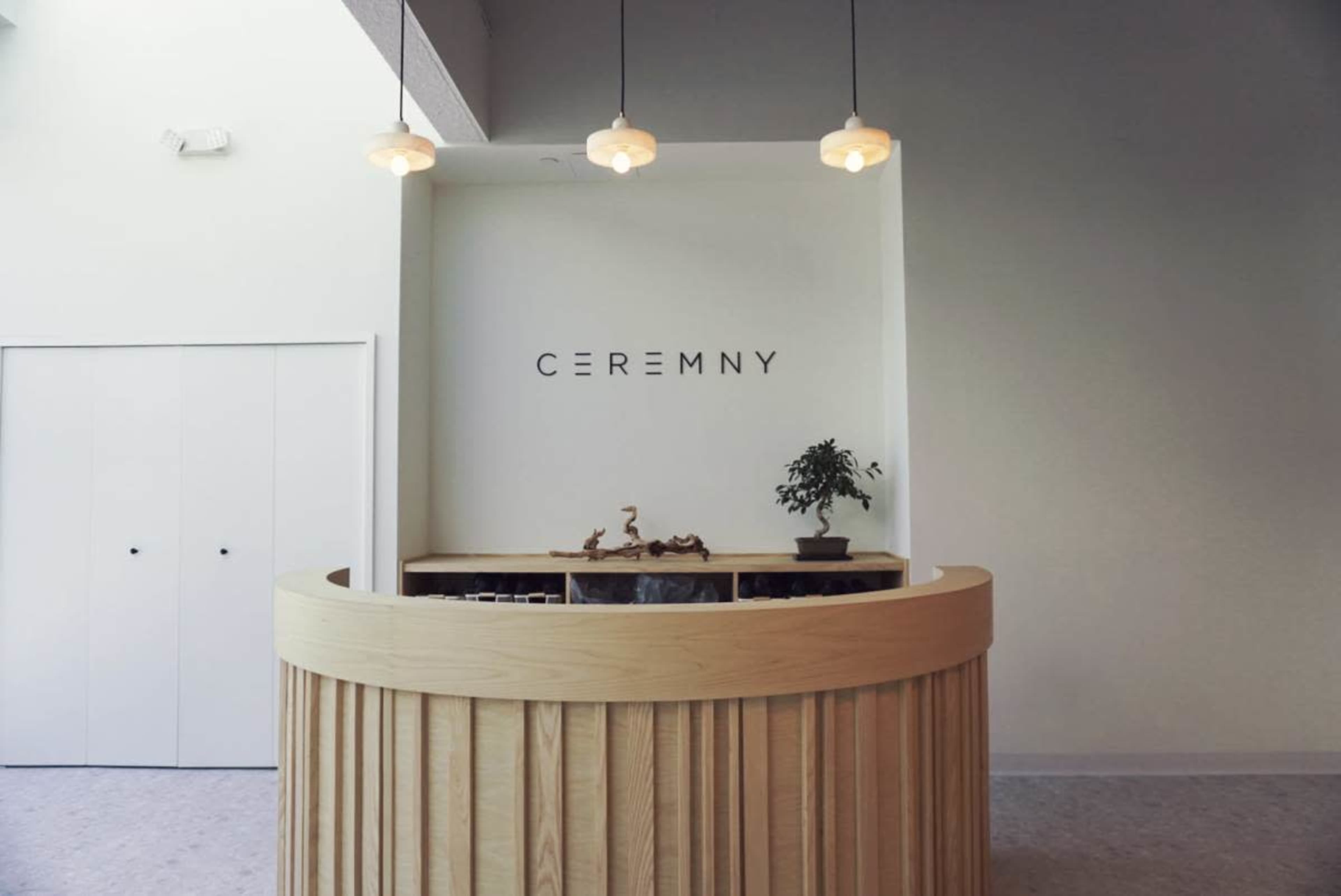The image depicts a modern reception area with a circular wooden front desk, featuring the word "CEREMNY" prominently displayed on the wall behind it.