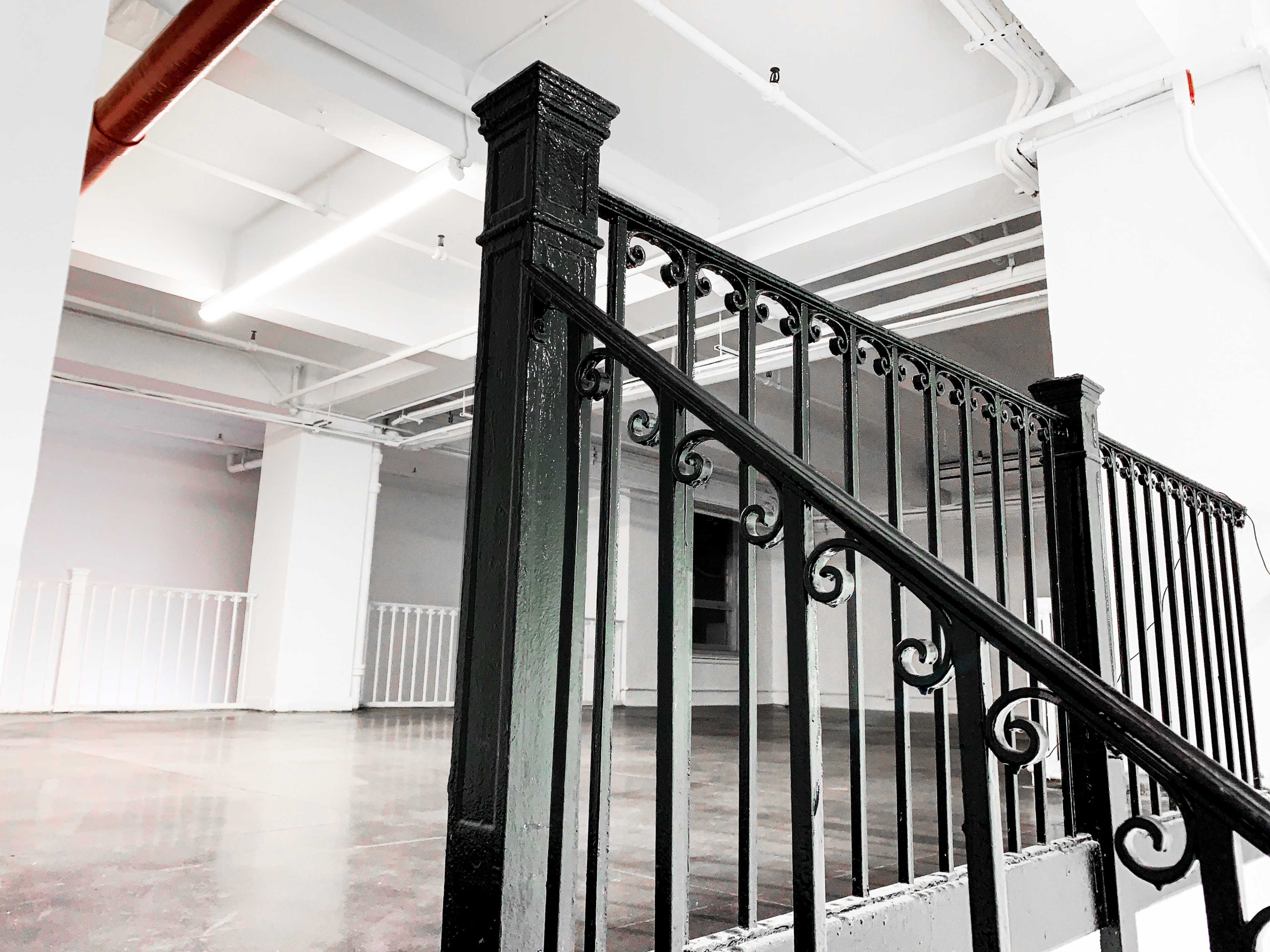 A black wrought iron staircase with decorative railings in a spacious, empty room with white walls and polished concrete floors.