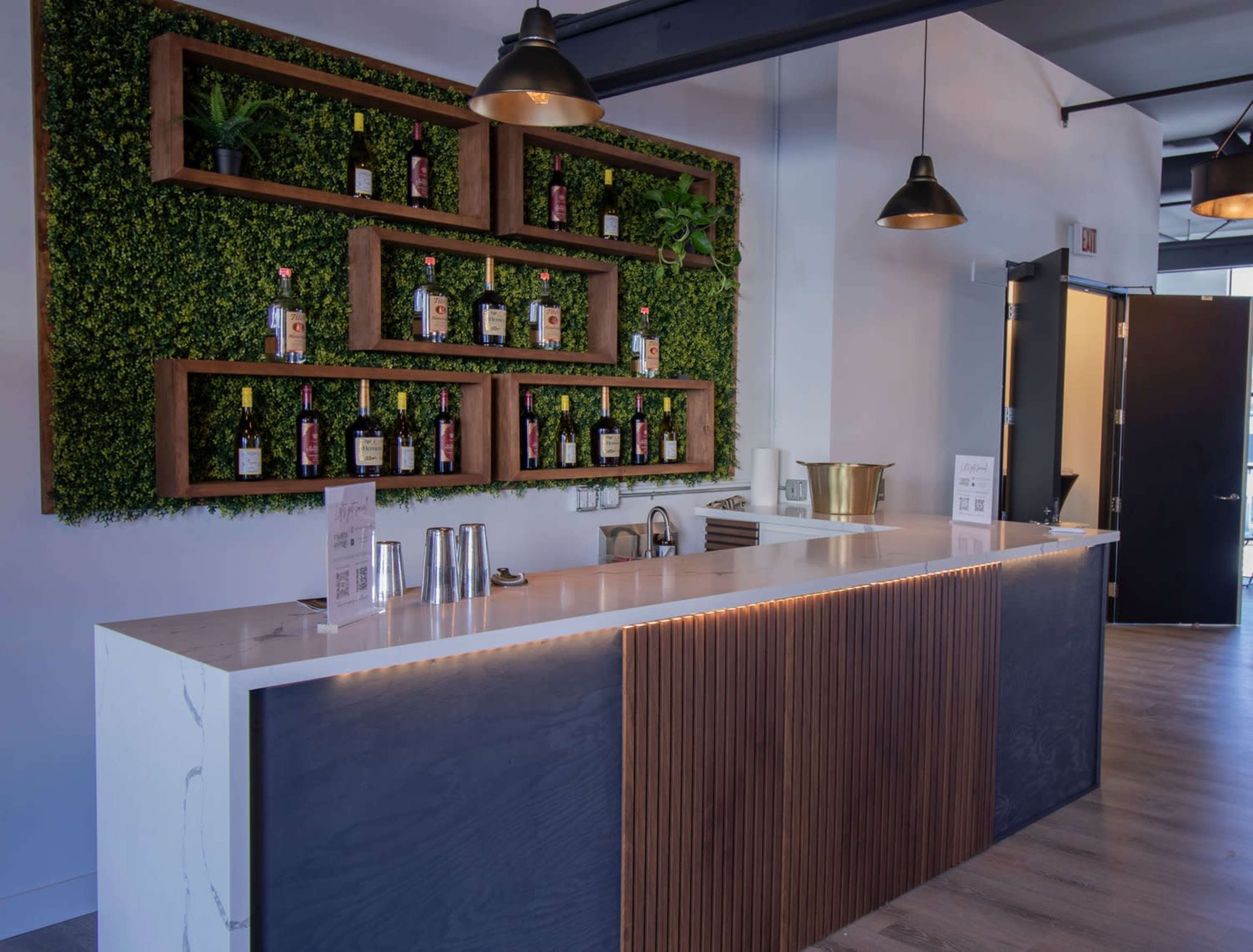 A modern bar with a wooden counter, a vertical garden wall displaying bottles, and pendant lighting.