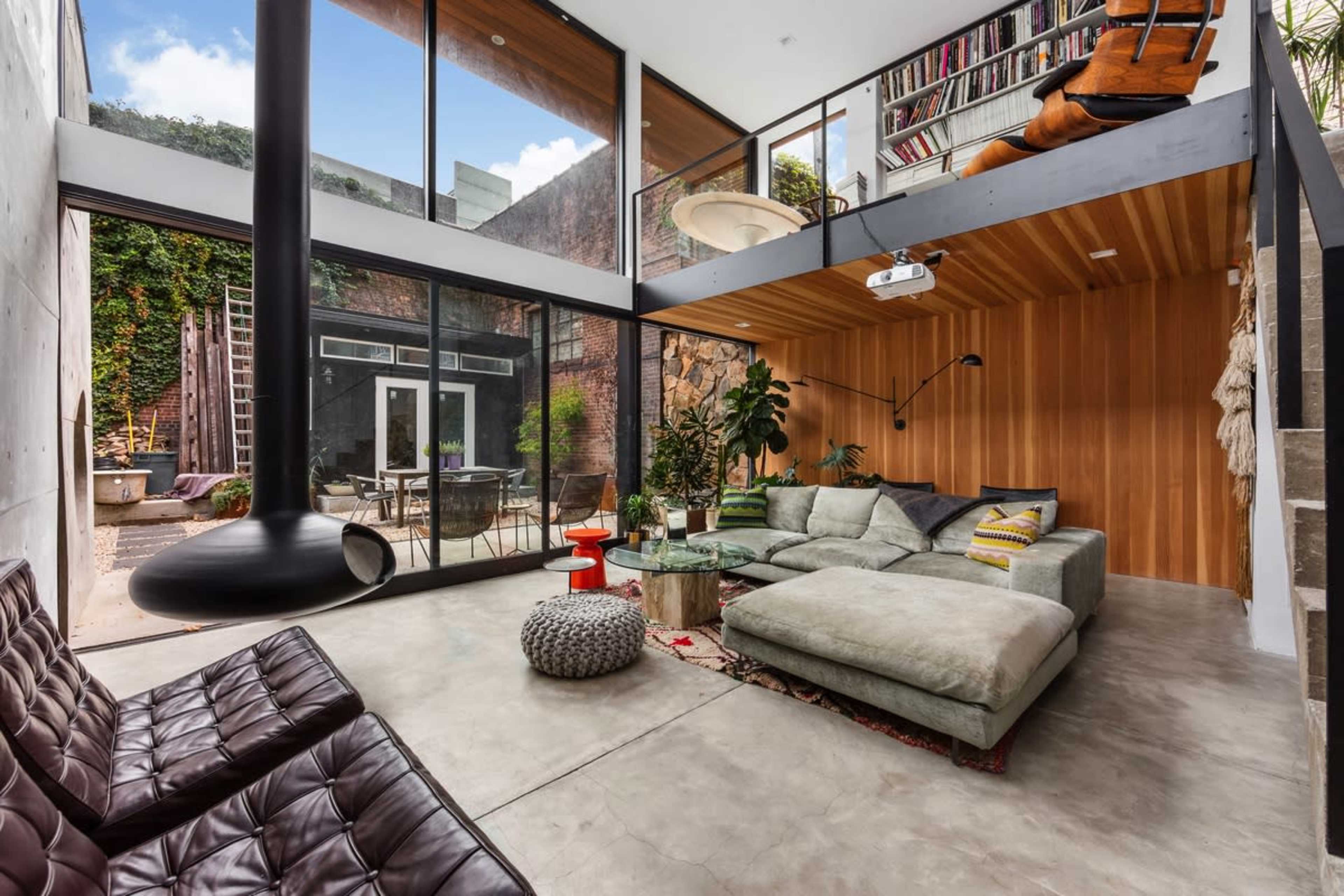 The image shows a modern living room featuring large glass windows, minimalistic furniture, and an open loft area with a staircase.