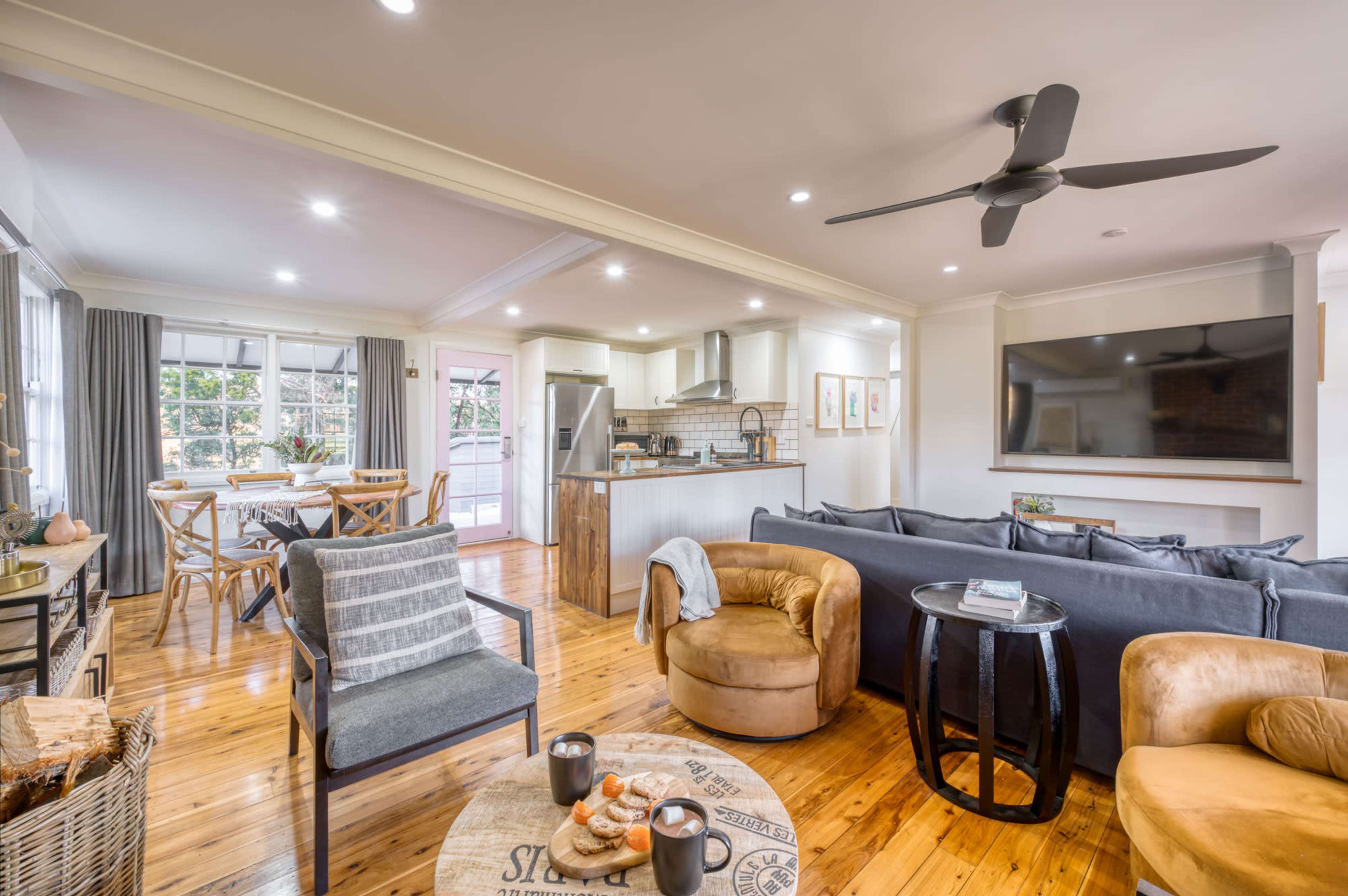 A modern living room and kitchen area with wooden floors, a large sofa, and a dining space with a table and chairs.