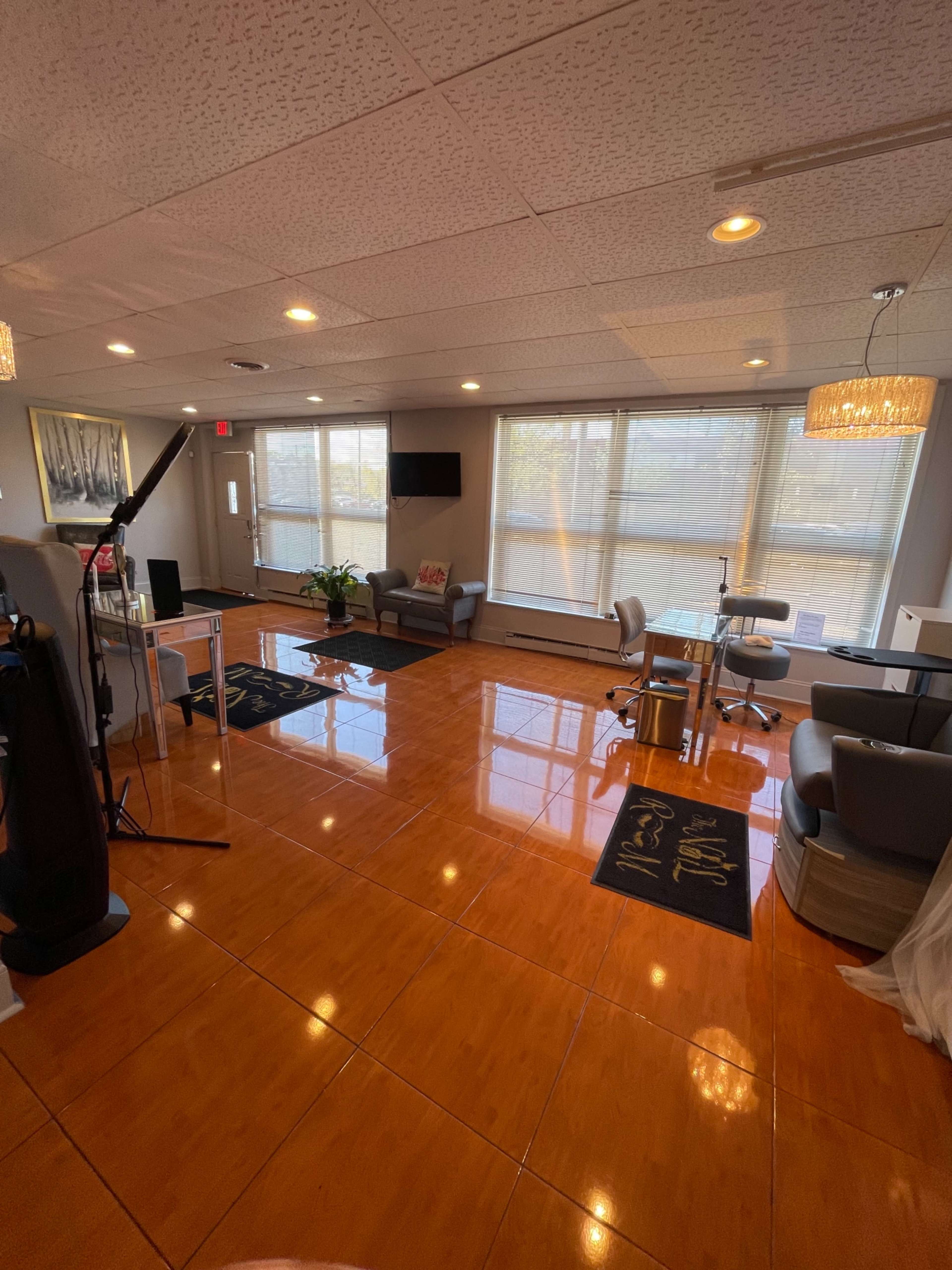 The image shows a well-lit salon or waiting area featuring a polished floor, comfortable seating, and large windows.