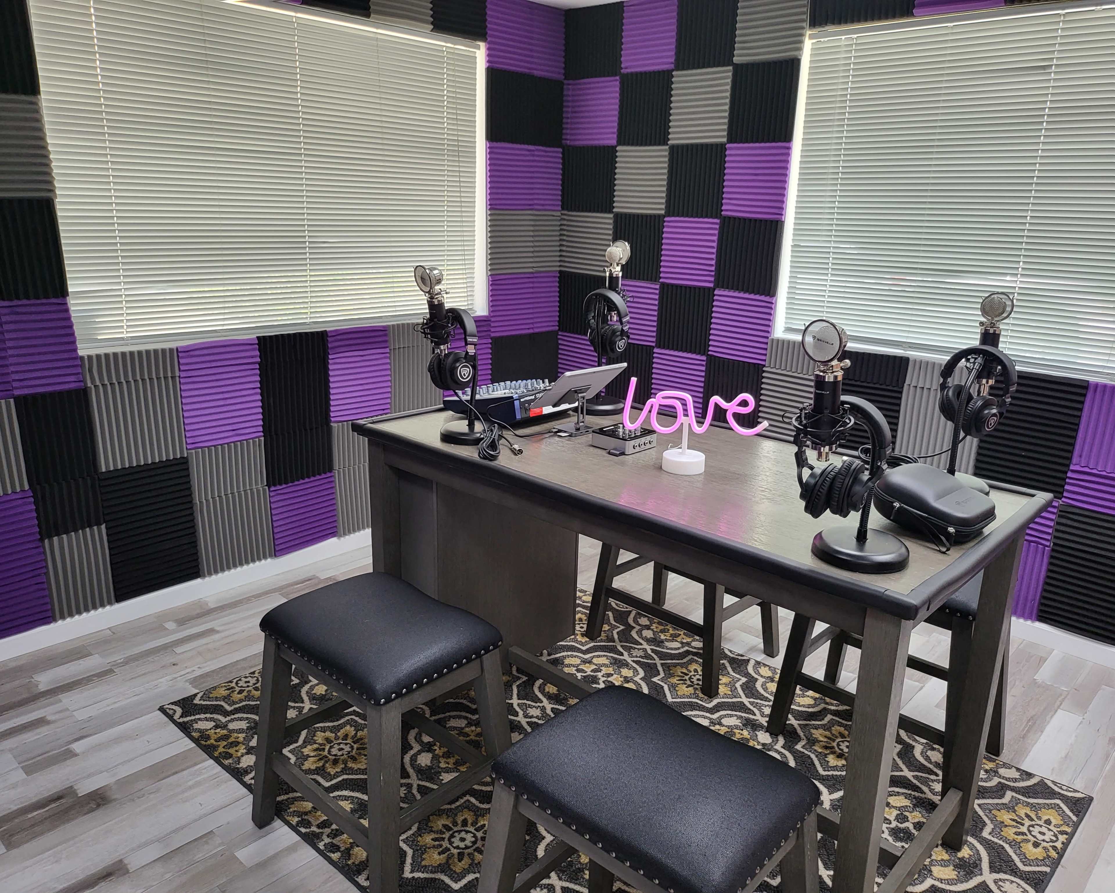 A recording studio with a table, four microphones, headphones, and purple and gray soundproofing panels on the walls.