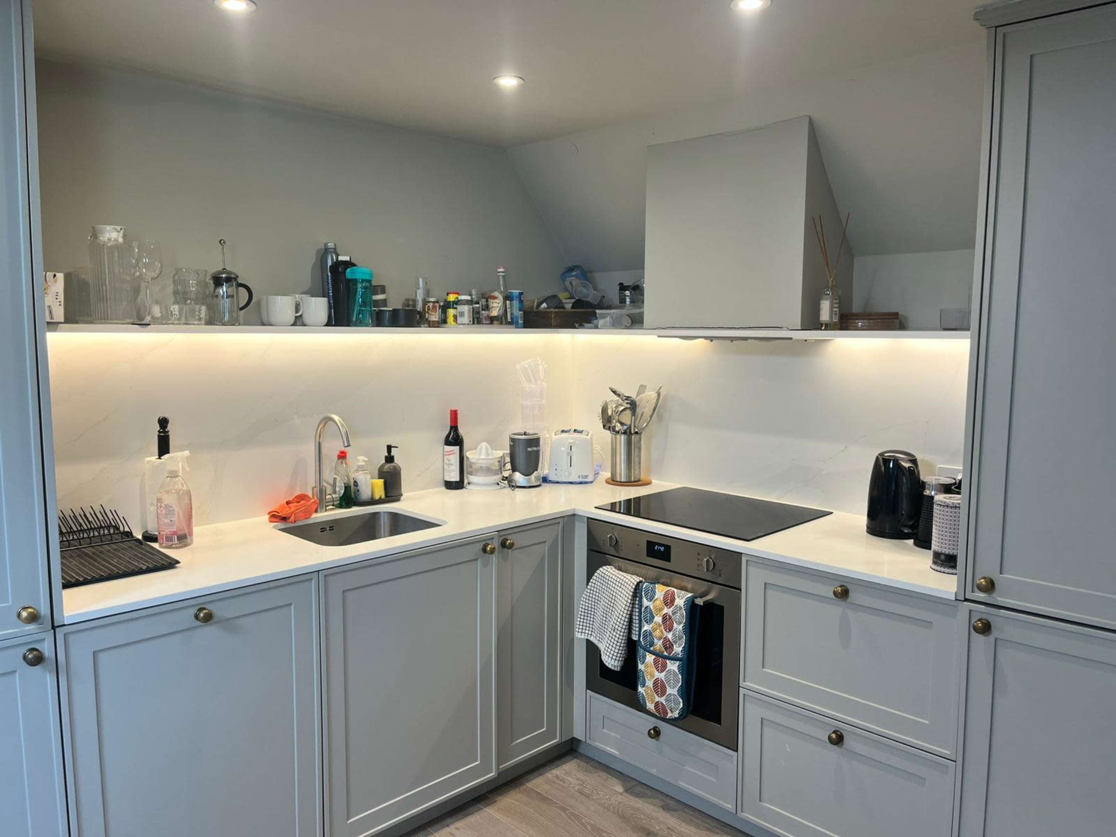 The image shows a modern kitchen with gray cabinetry, a sink, an oven, and various kitchen appliances on the countertops.