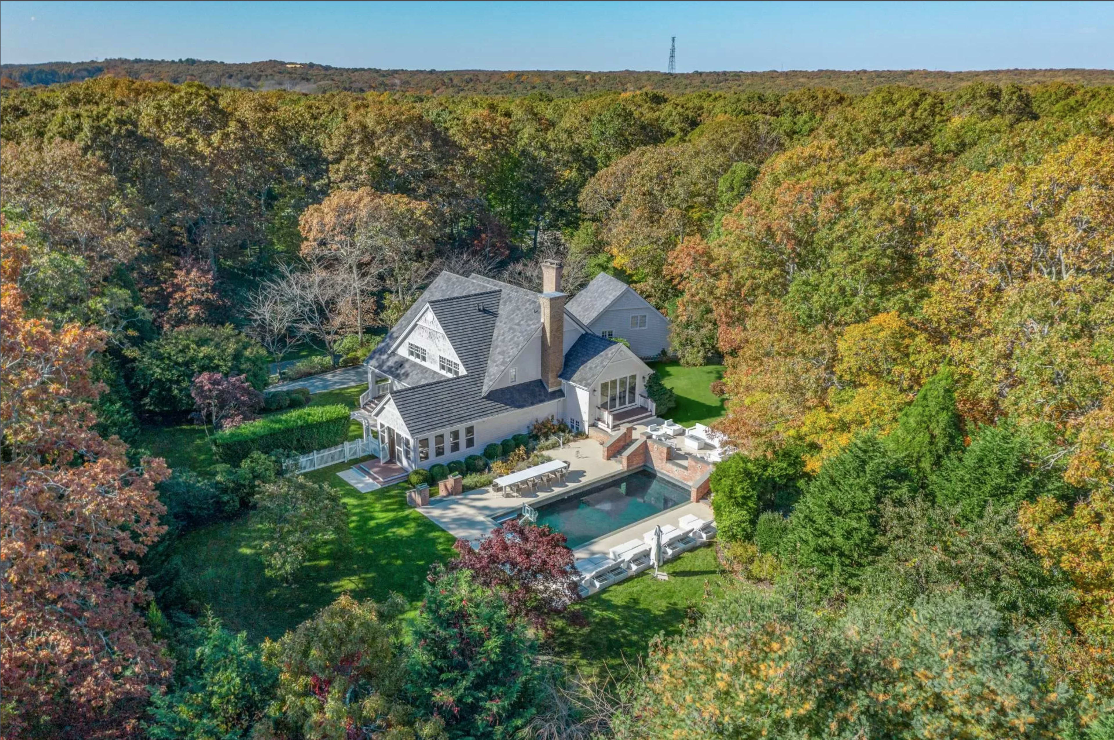 A large house surrounded by colorful trees and a landscaped yard featuring a swimming pool and patio area.