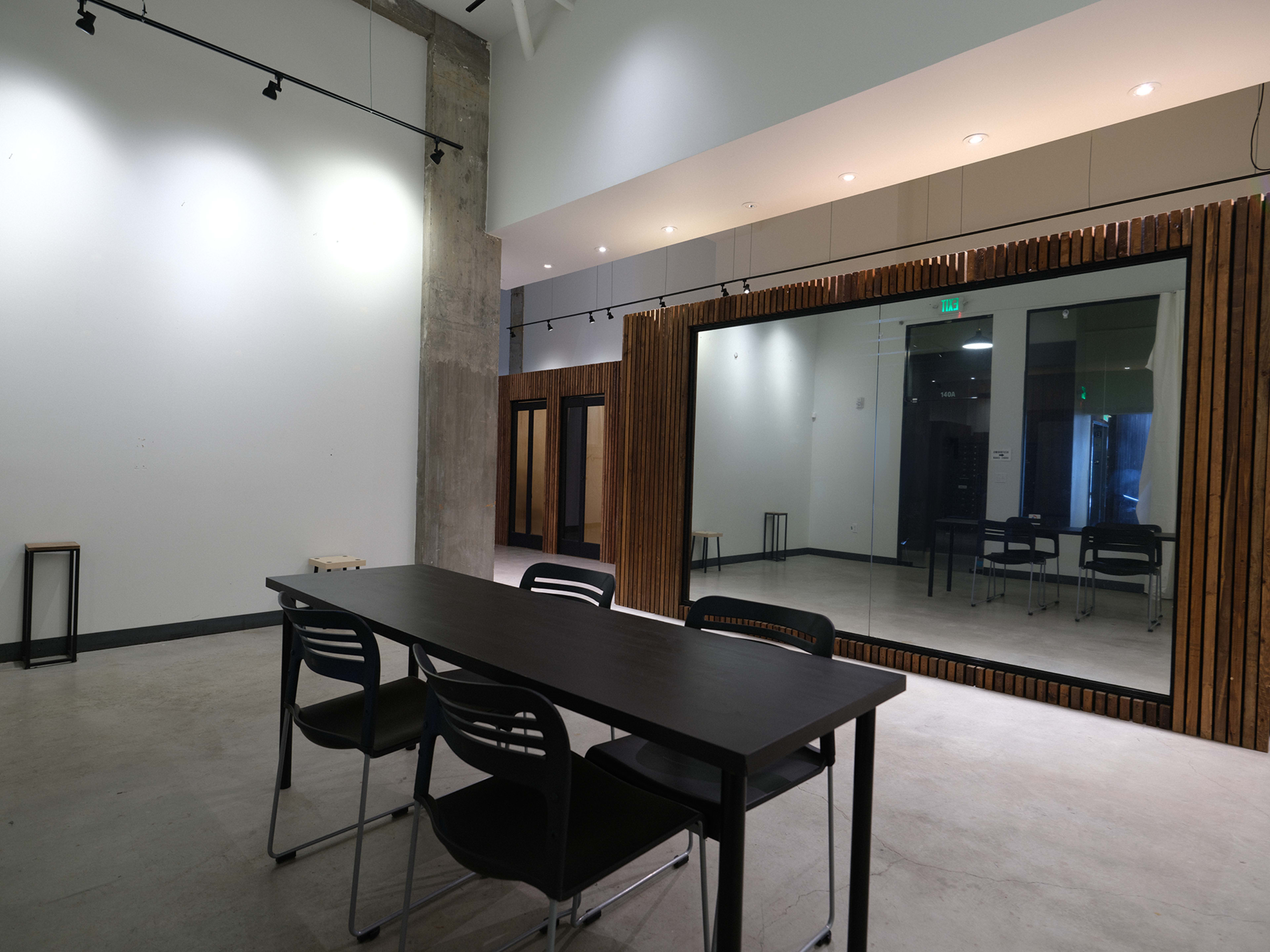 The image shows a minimalistic interior space featuring a black table with six chairs, large mirrored paneling, and a concrete wall.