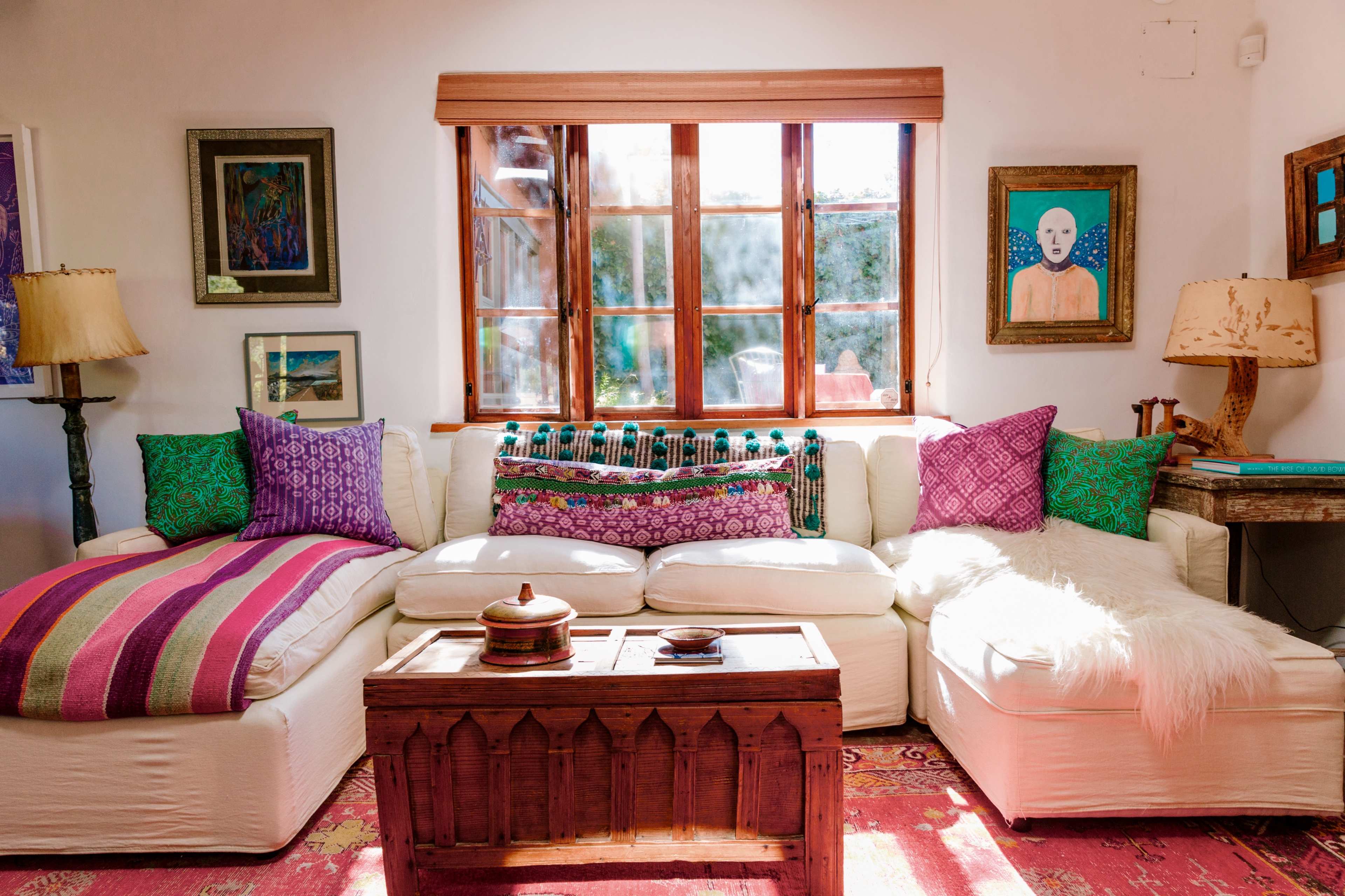 The scene shows a bright living room featuring a white sectional sofa adorned with colorful cushions and a wooden coffee table in front.
