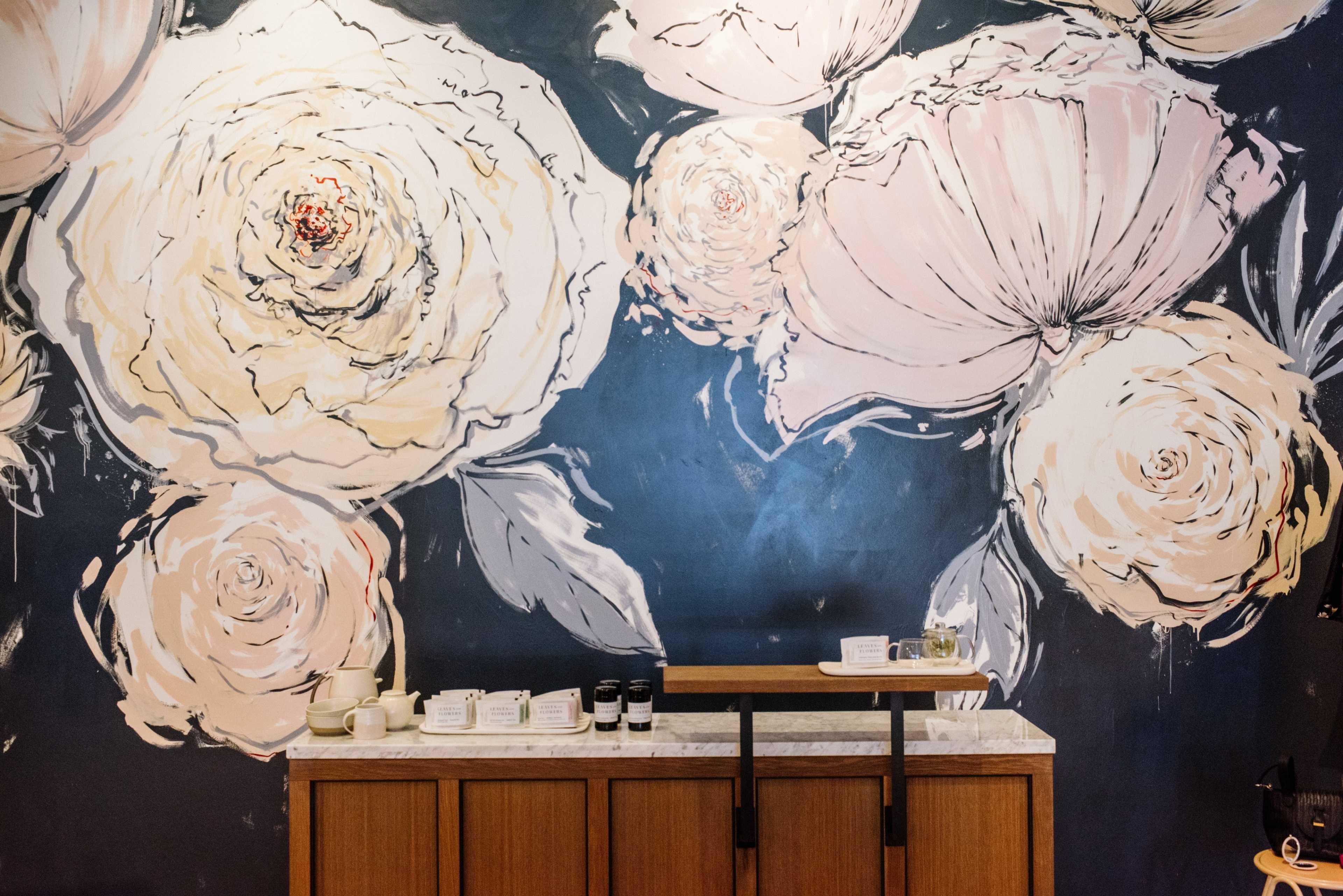 A wooden counter in front of a large mural featuring oversized, light-colored floral designs against a dark background.
