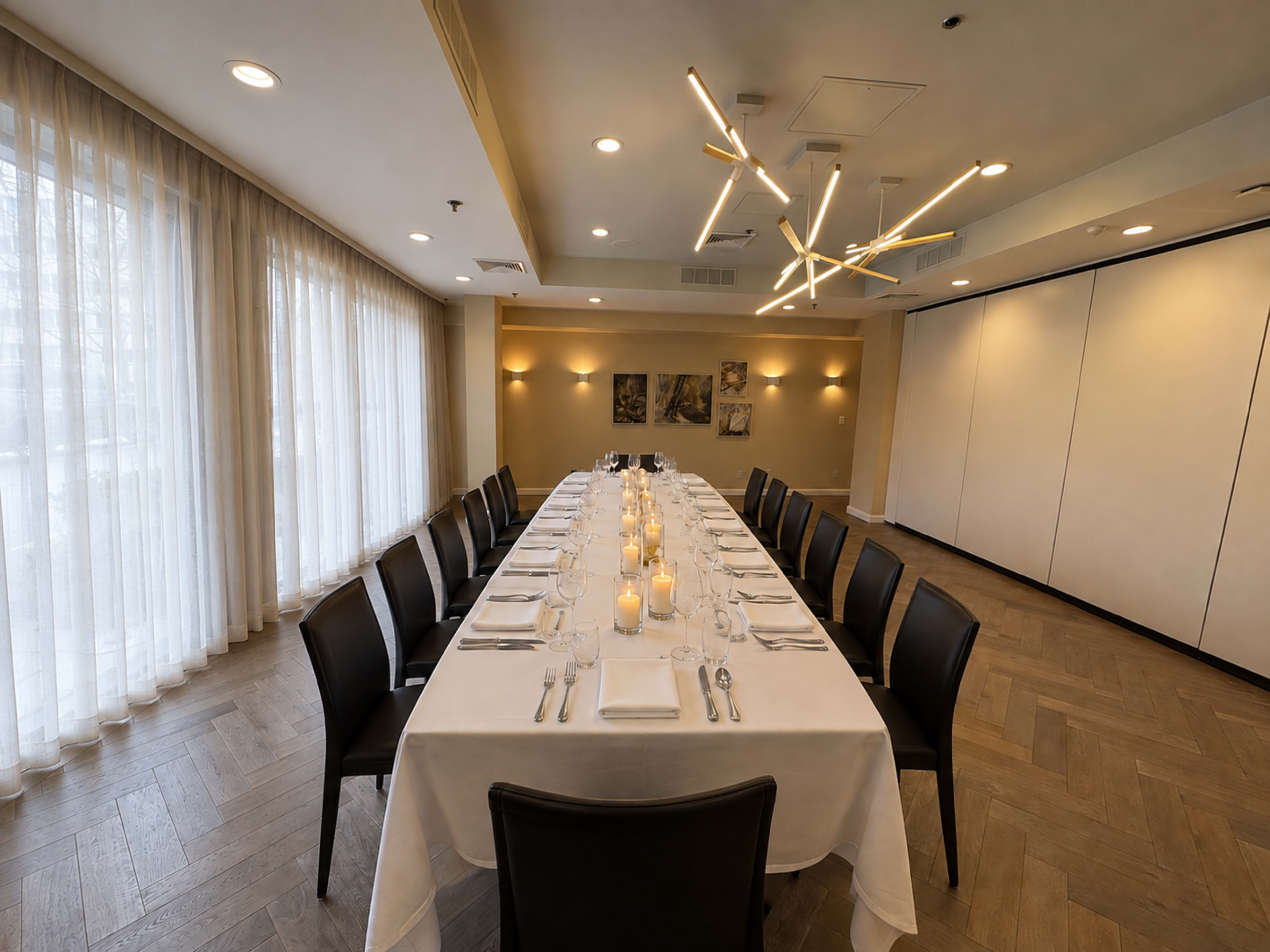 The image shows a long dining table set with white linens and candles in a well-lit private dining room.