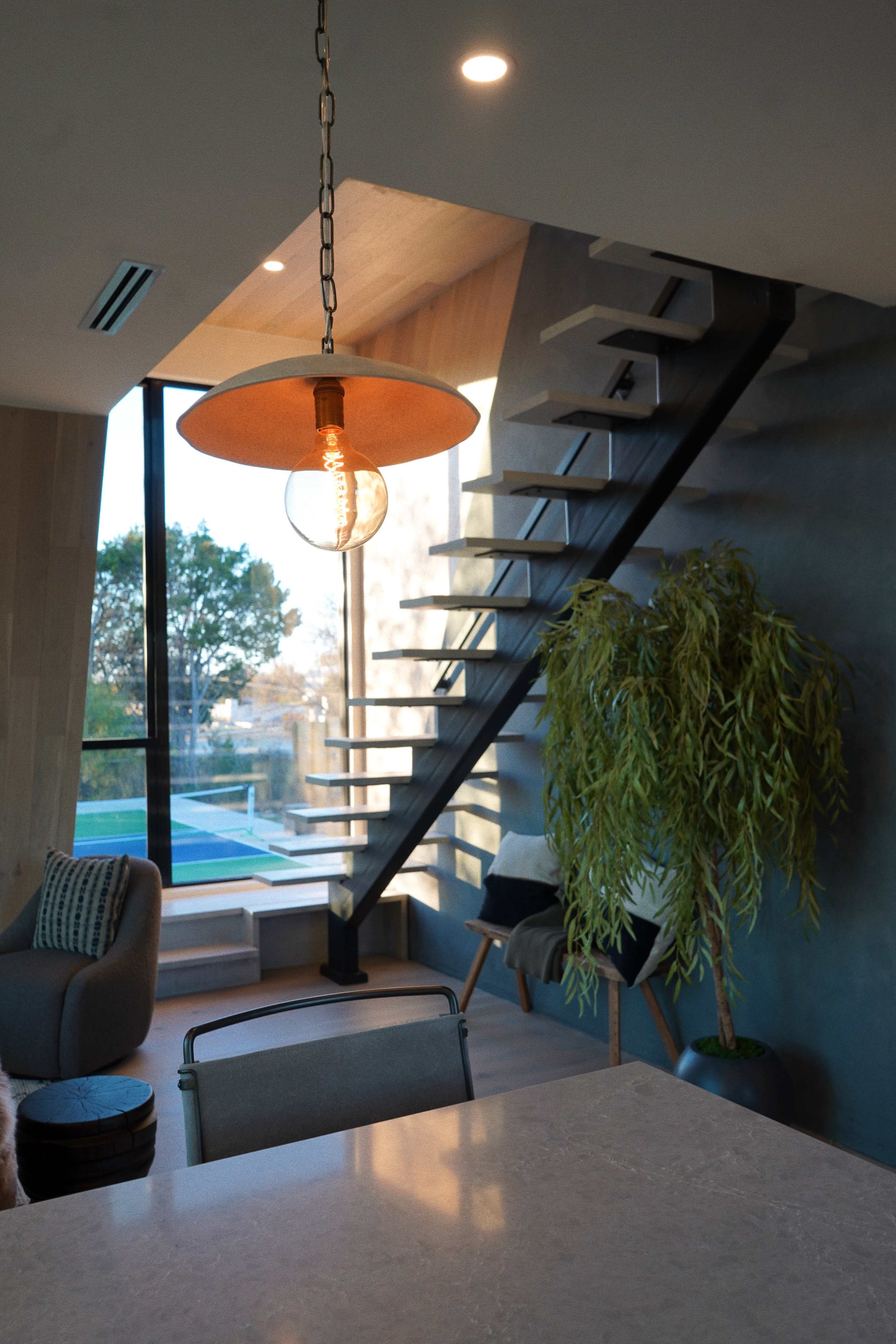 A modern interior featuring a staircase with a pendant lamp, a potted plant, and a view of a pool through large windows.