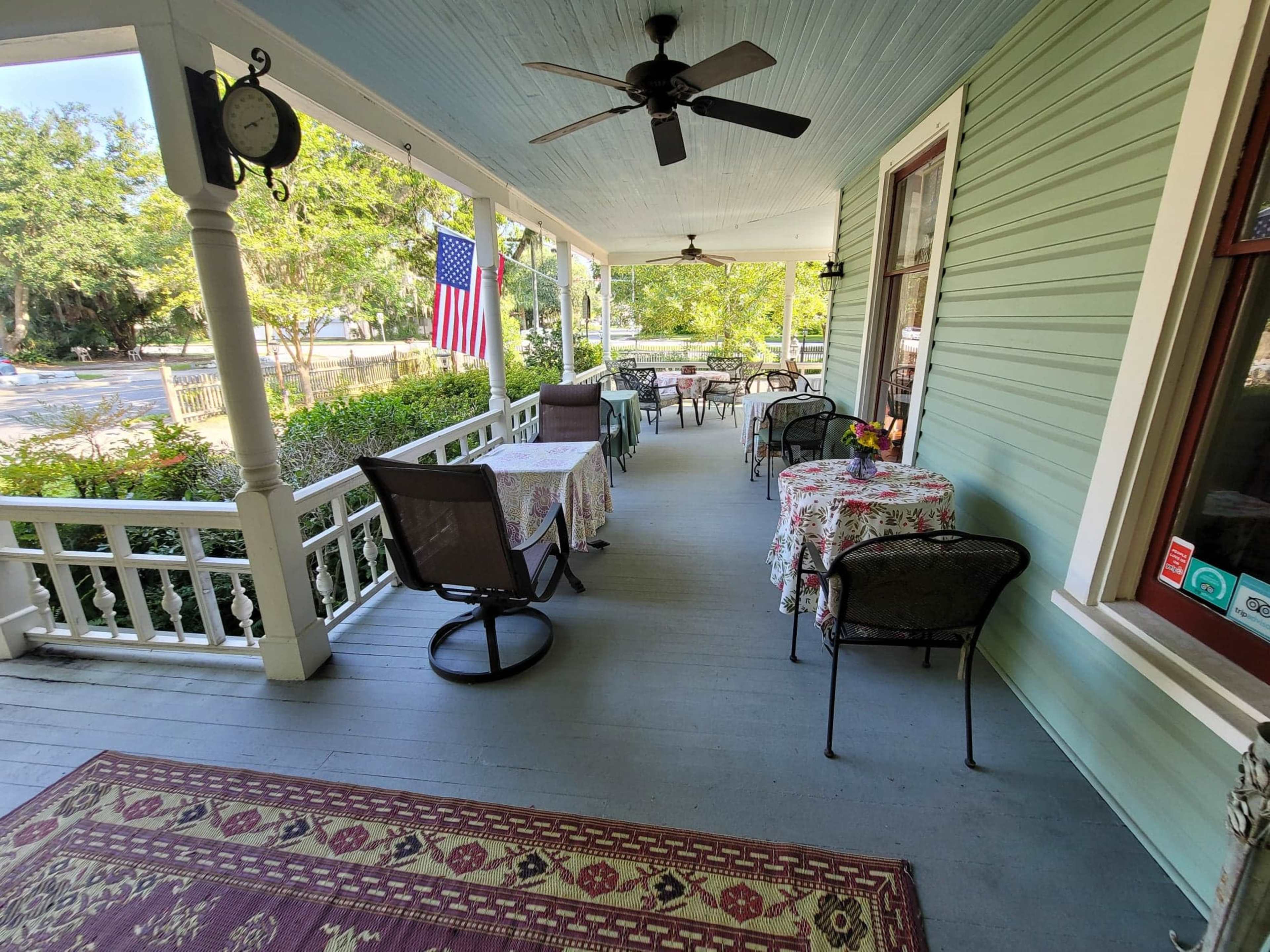 A porch with several tables and chairs, decorated with patterned tablecloths, and an American flag hanging prominently.