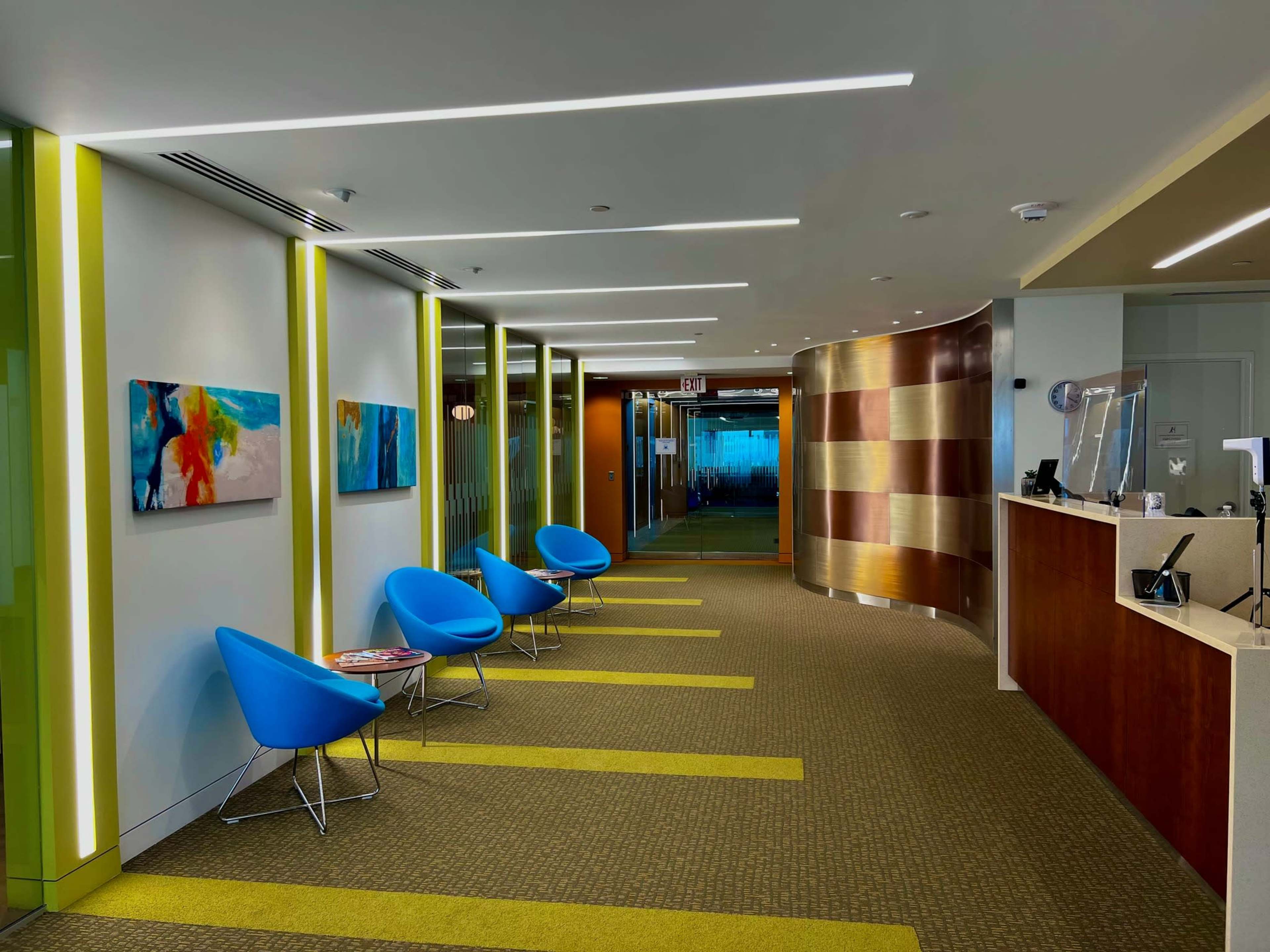 A modern office reception area with blue chairs, striped wall accents, and a reception desk.